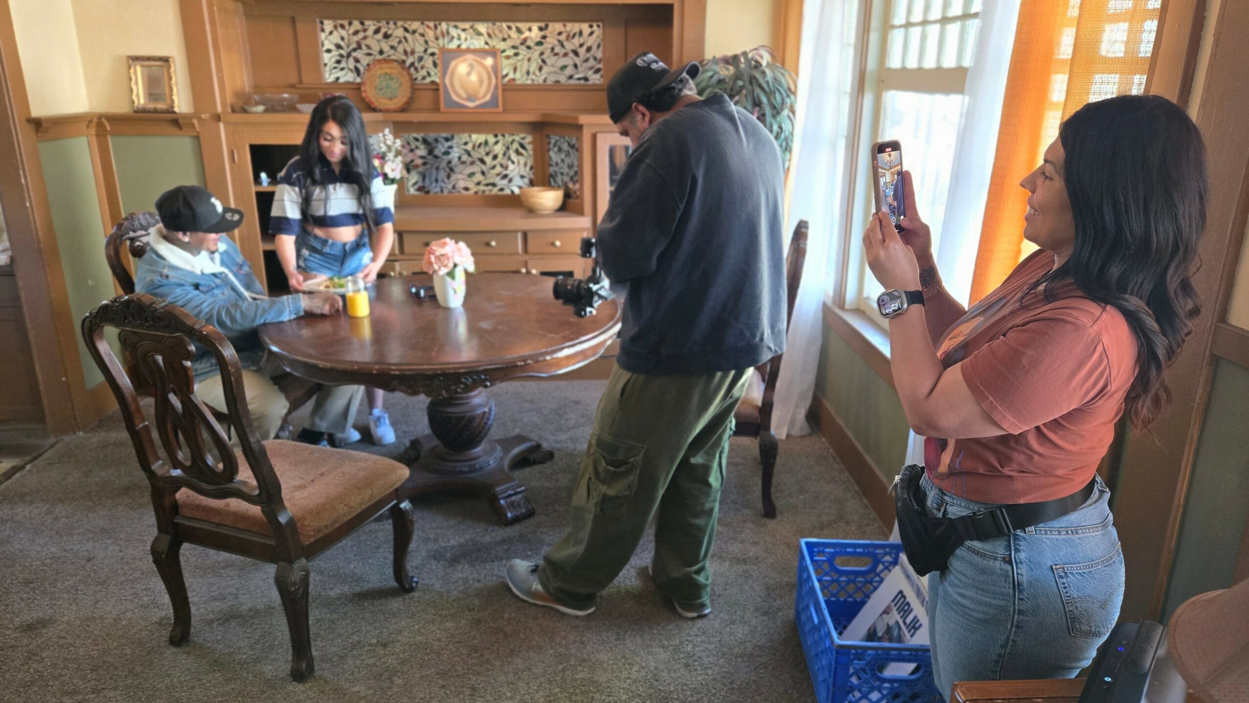 People gathered around a dining table in a room with wooden furniture and a window with curtains.