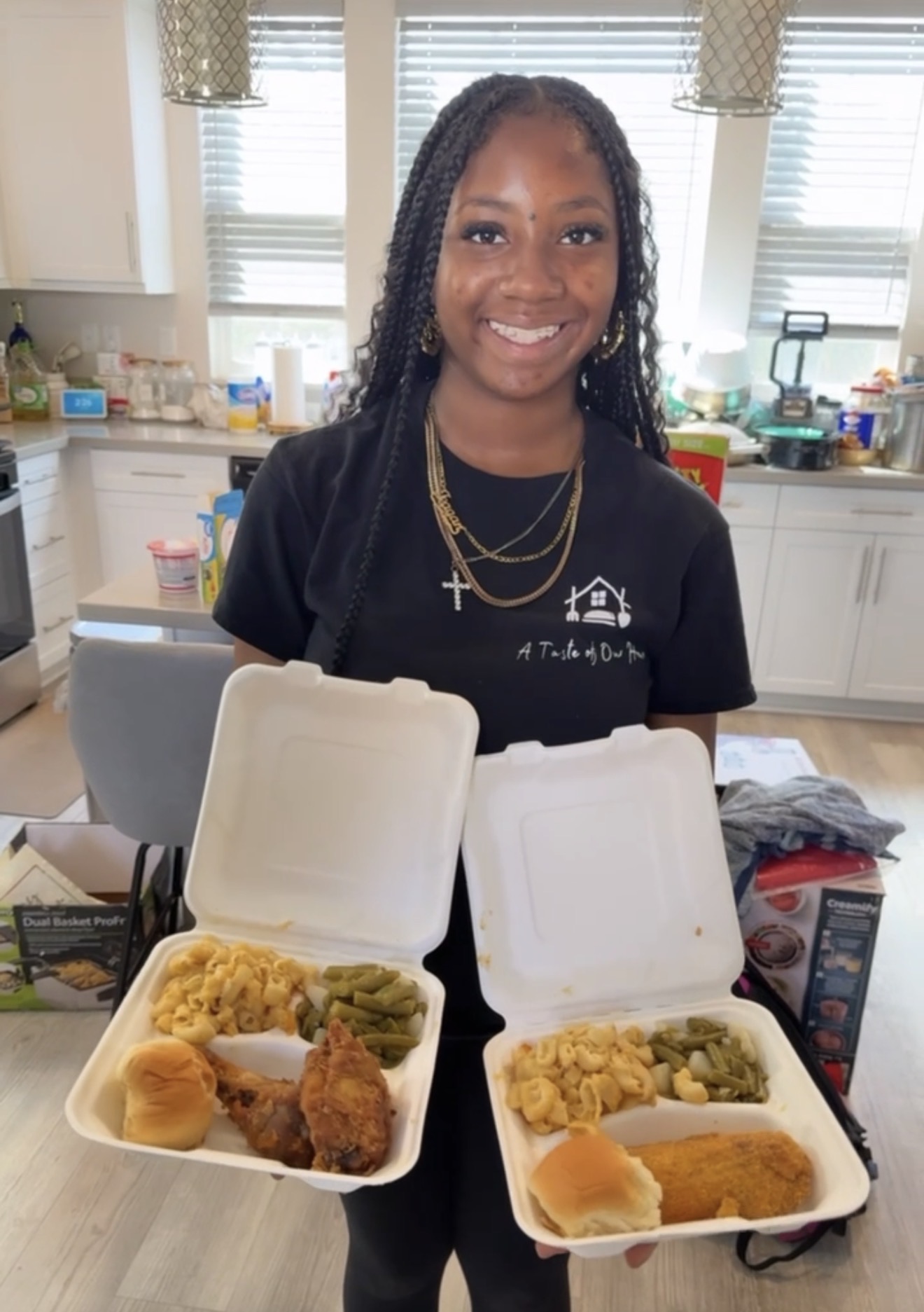 Smiling girl with braided hair standing behind open takeout containers of food in a kitchen.