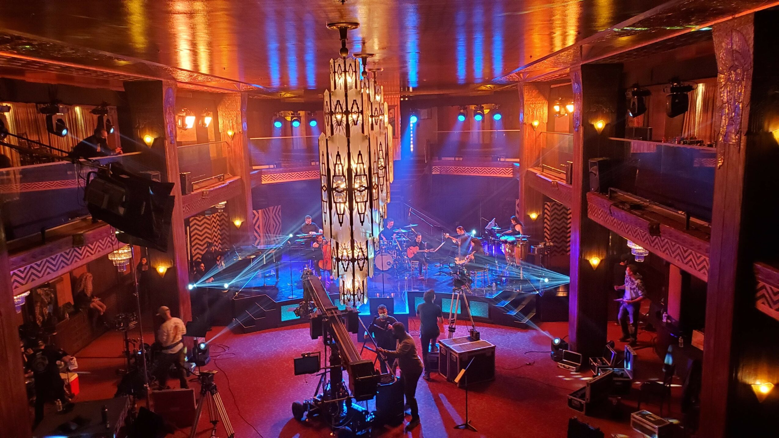 Concert stage with musicians, colorful lighting, and audience in a large, elegant hall.