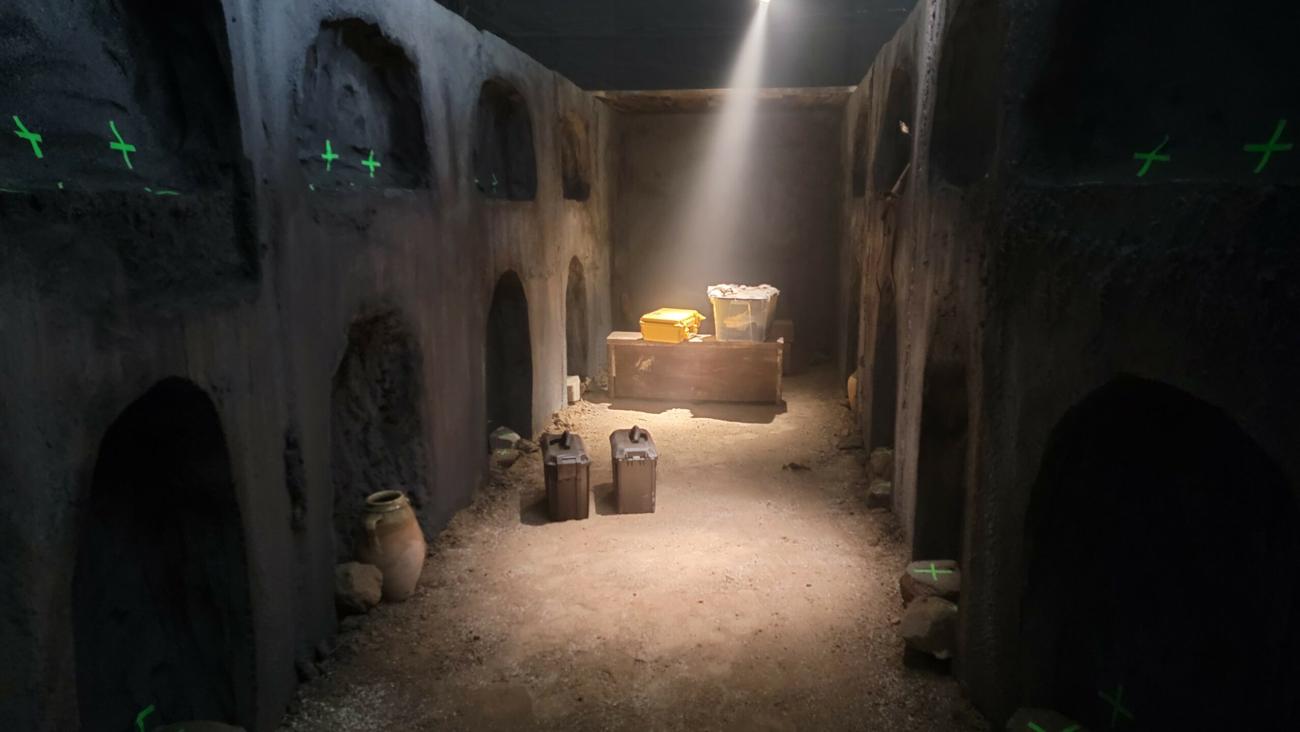 Underground catacomb with arched niches, dim lighting, and scattered objects on the ground.