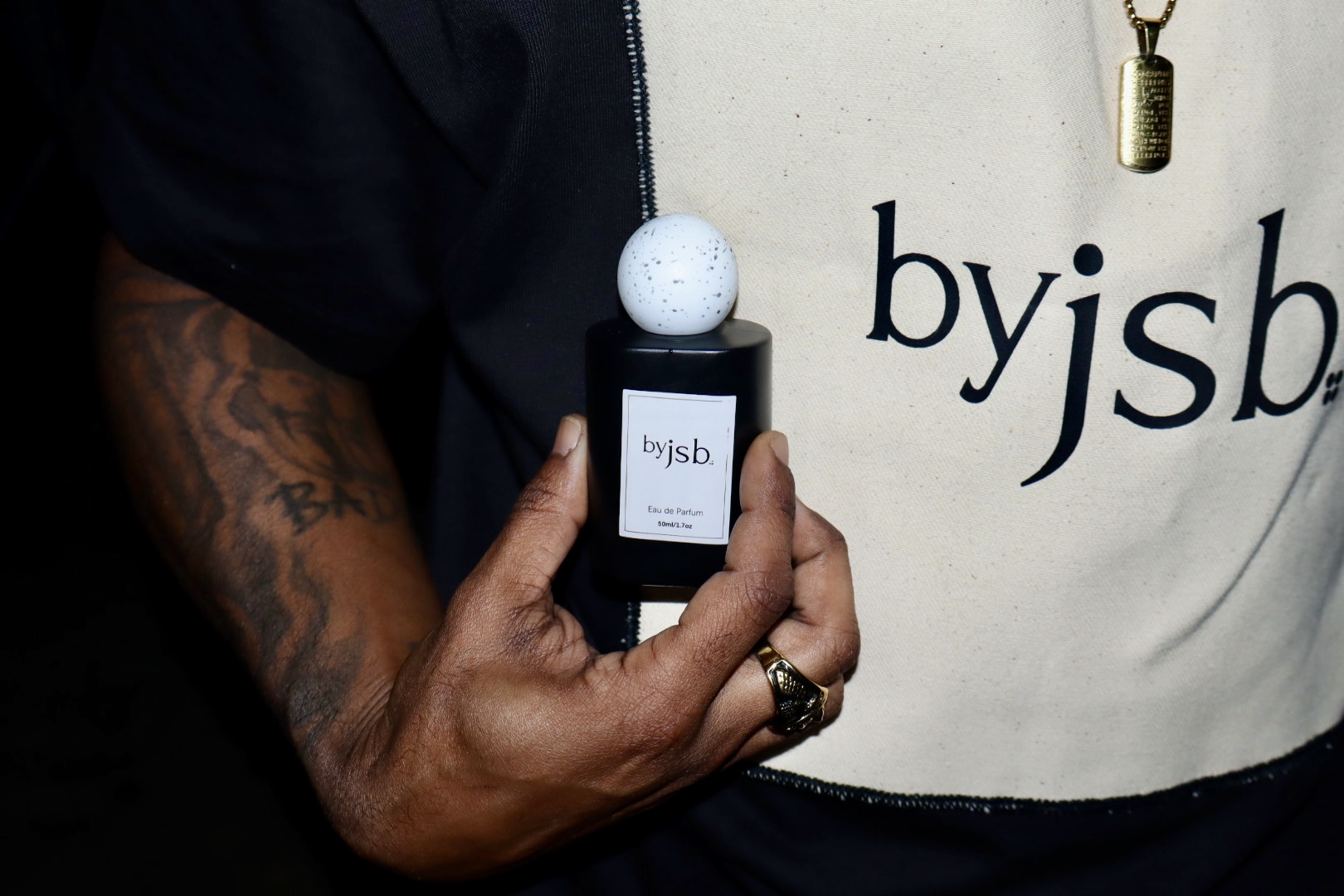 Person holding a small black bottle with a white ball on top, wearing a white shirt with black text.