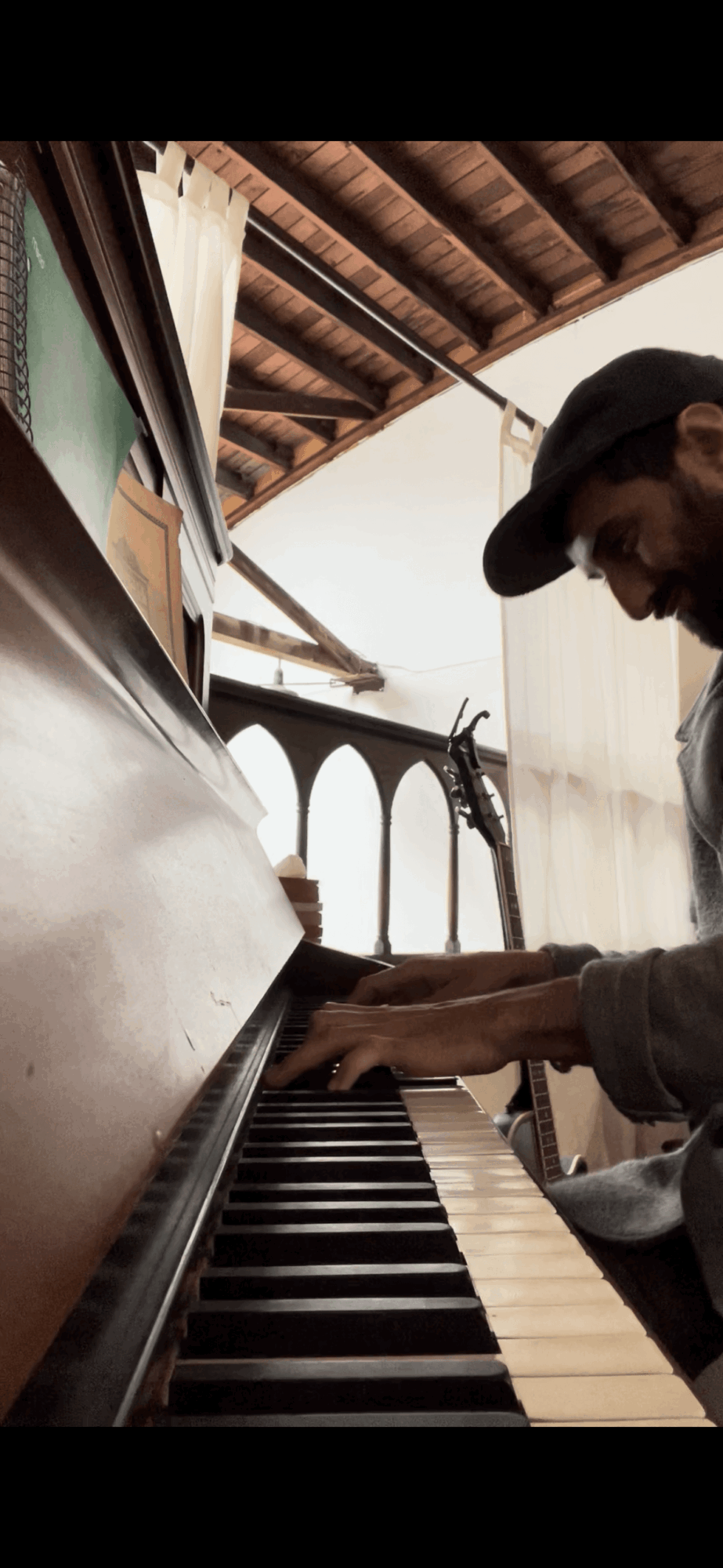 Person playing piano indoors, with wooden ceiling and window in background.