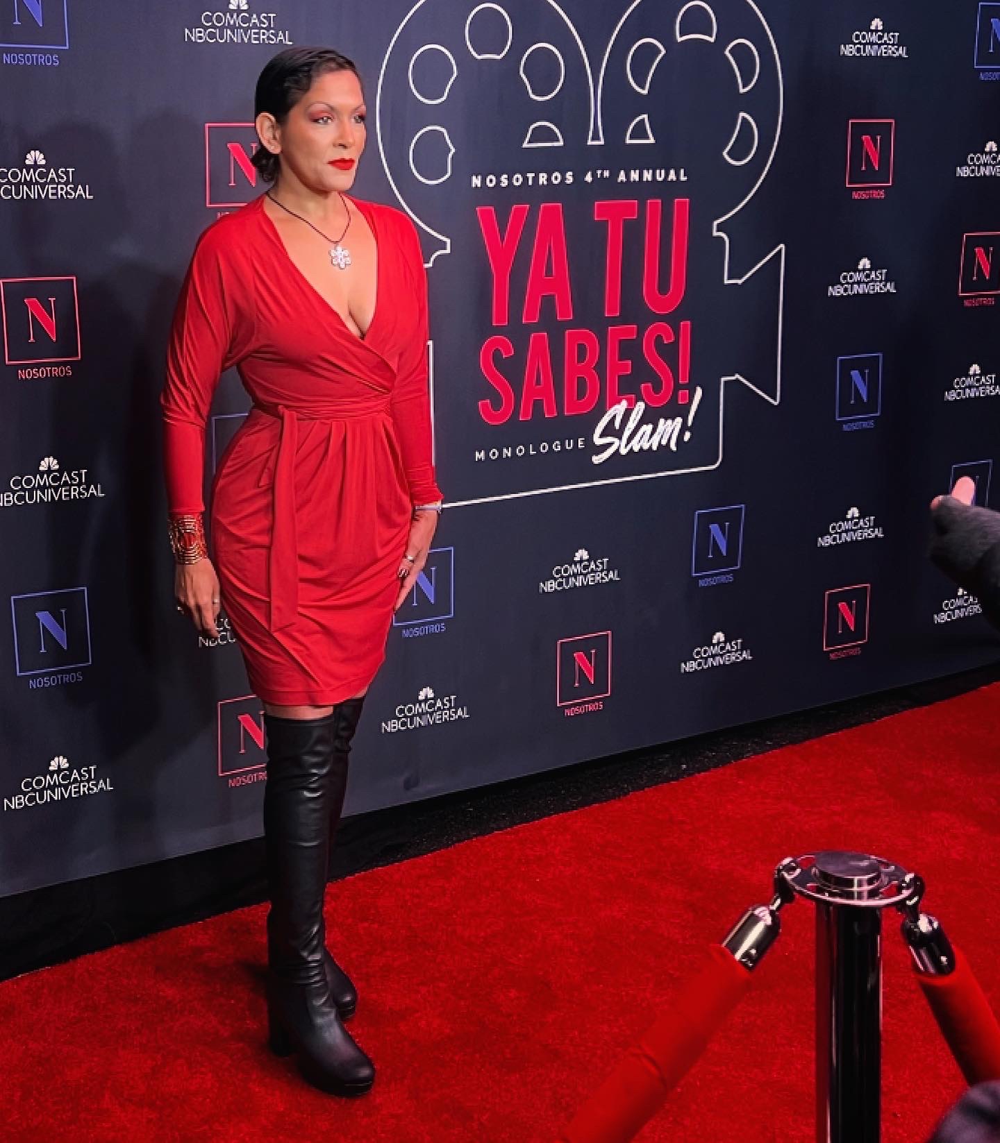 Woman in red dress and black boots standing on red carpet at event with Netflix backdrop, speech bubble graphic, and text.