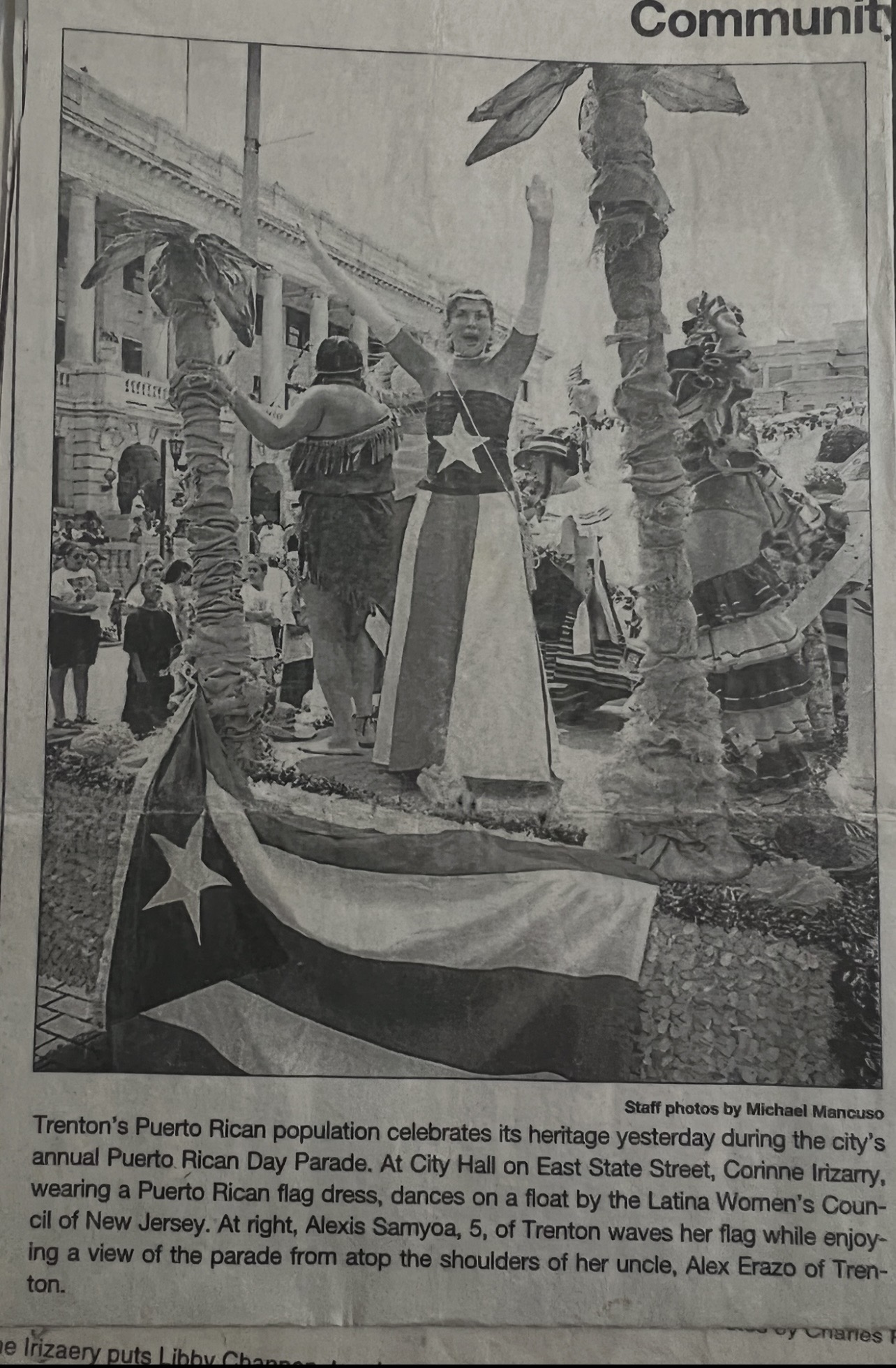 People celebrating Puerto Rican Day Parade with a woman in traditional dress, Puerto Rican flags, and a crowd in the background.