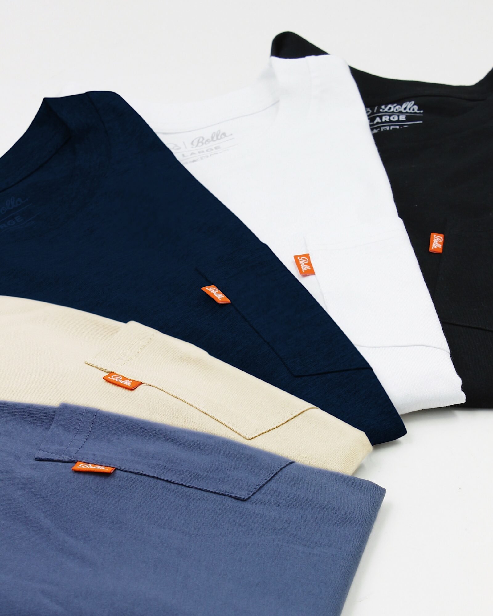Four folded T-shirts in navy, white, black, and light blue, with small orange tags visible, arranged on a flat surface.