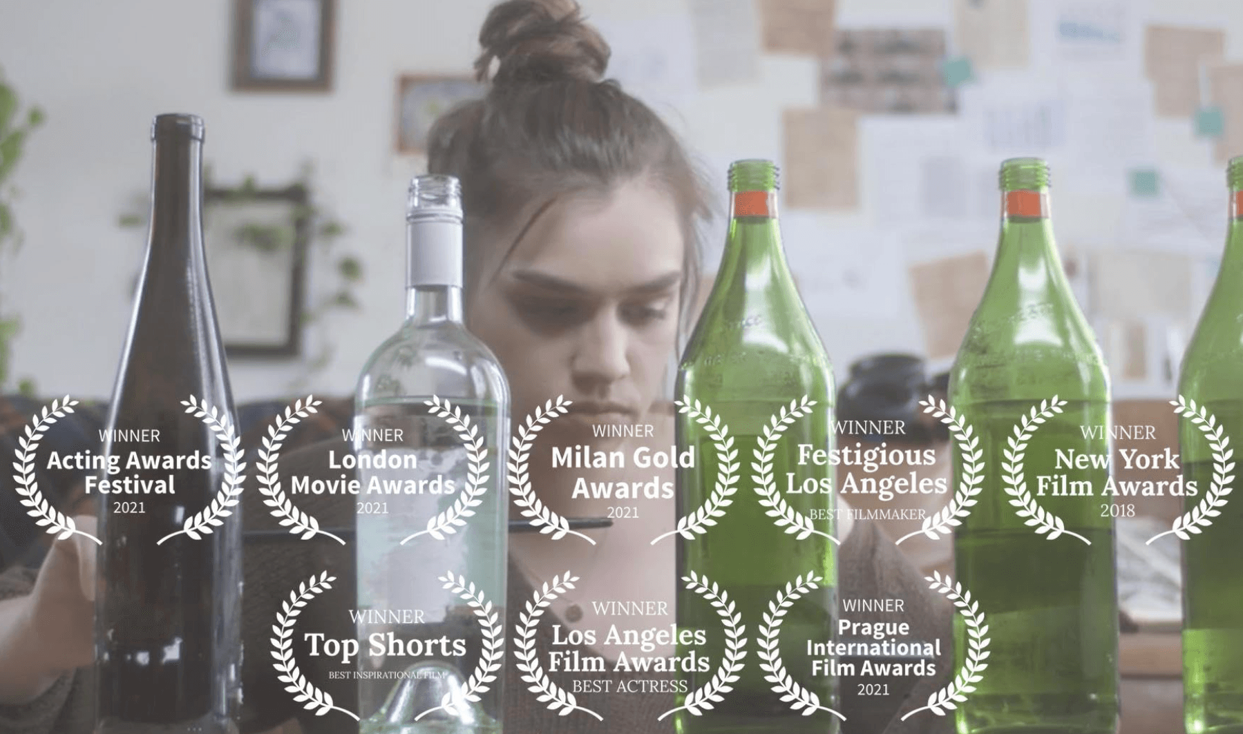 A woman with a bun hairstyle sits at a table with three green bottles, with award logos overlayed on the image.