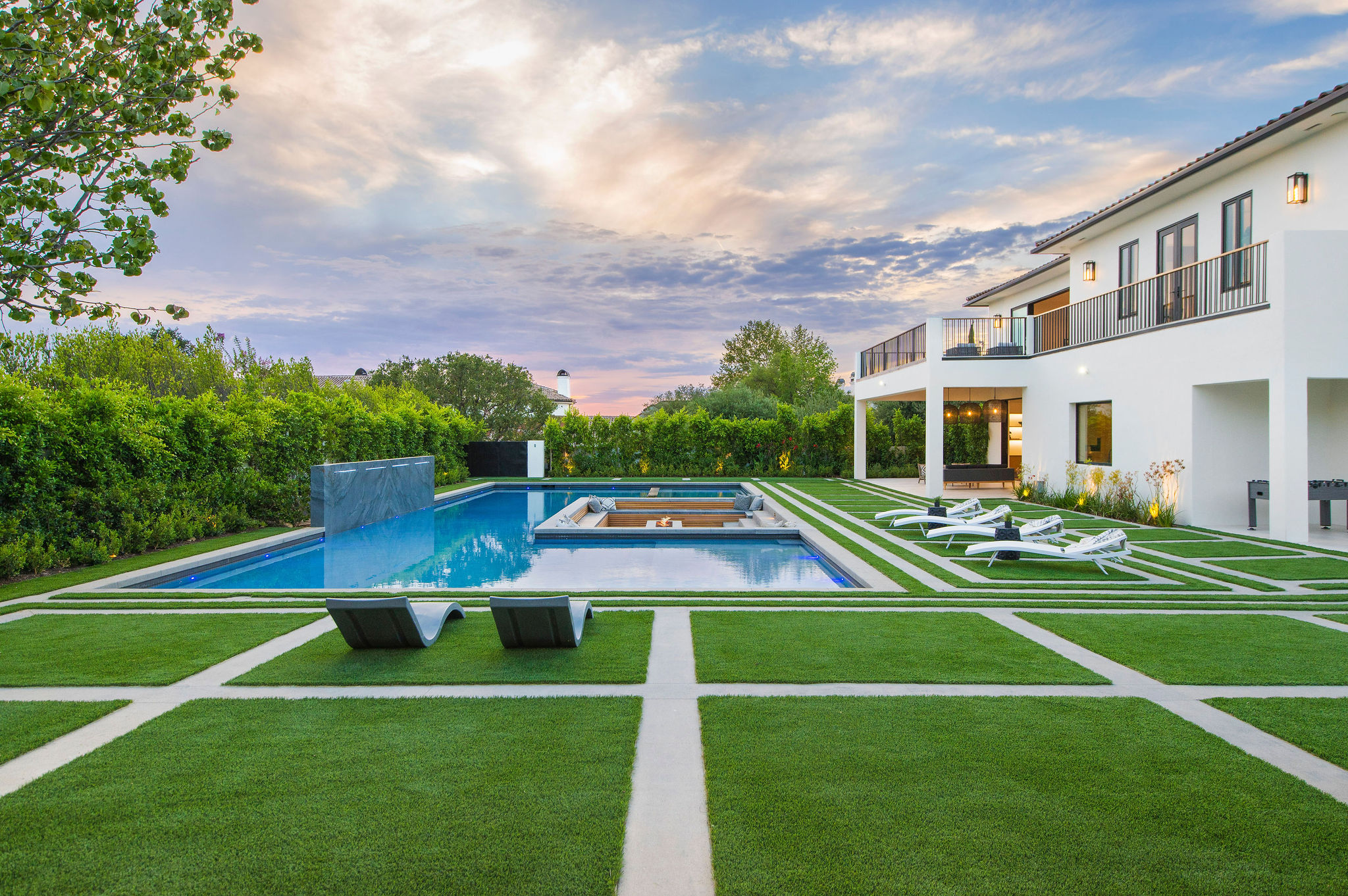 Modern house with a swimming pool, lounge chairs, and a well-maintained lawn under a partly cloudy sky.