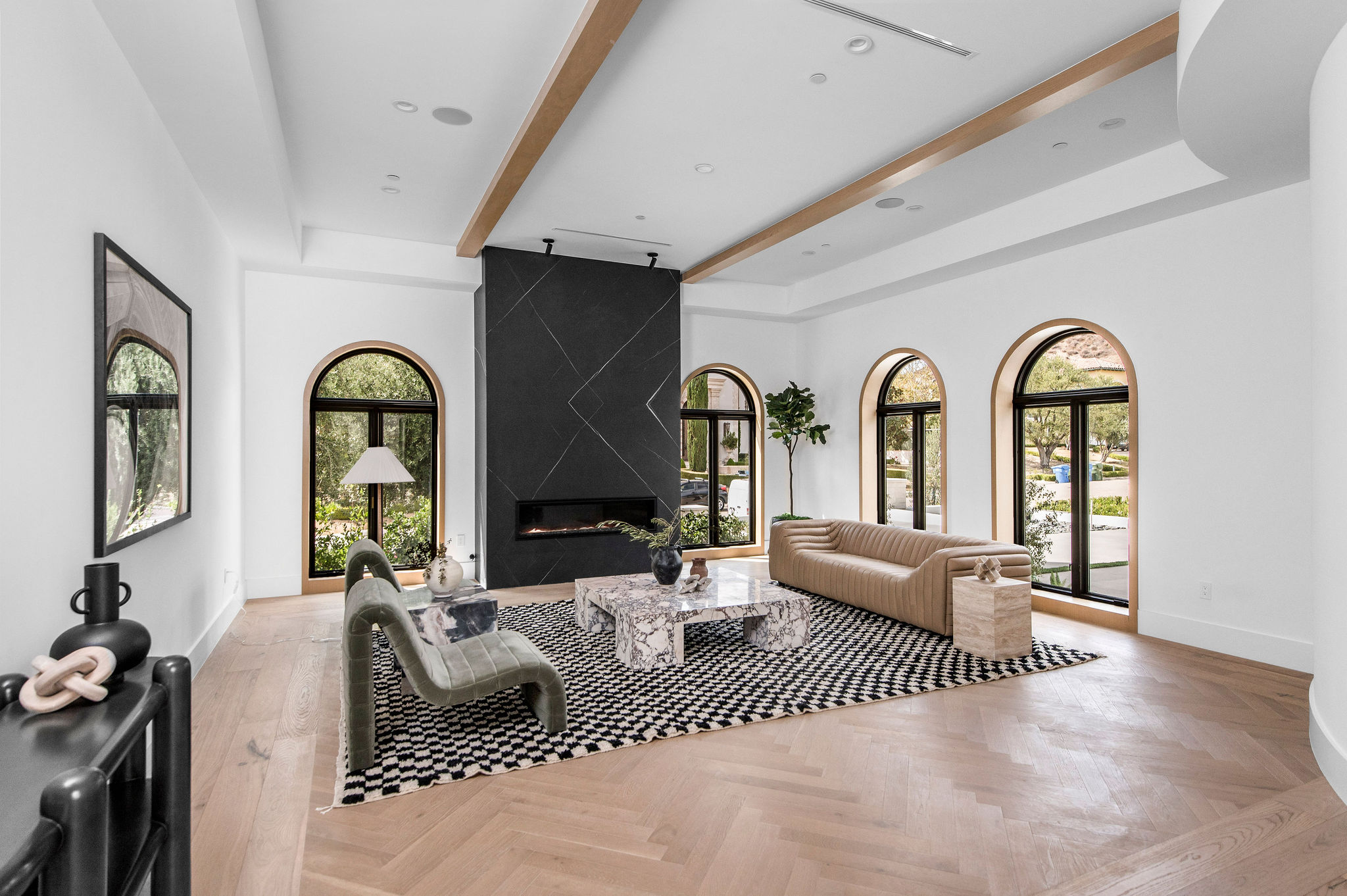 Living room with large arched windows, a black fireplace, a beige sofa, a patterned rug, and a gray armchair.