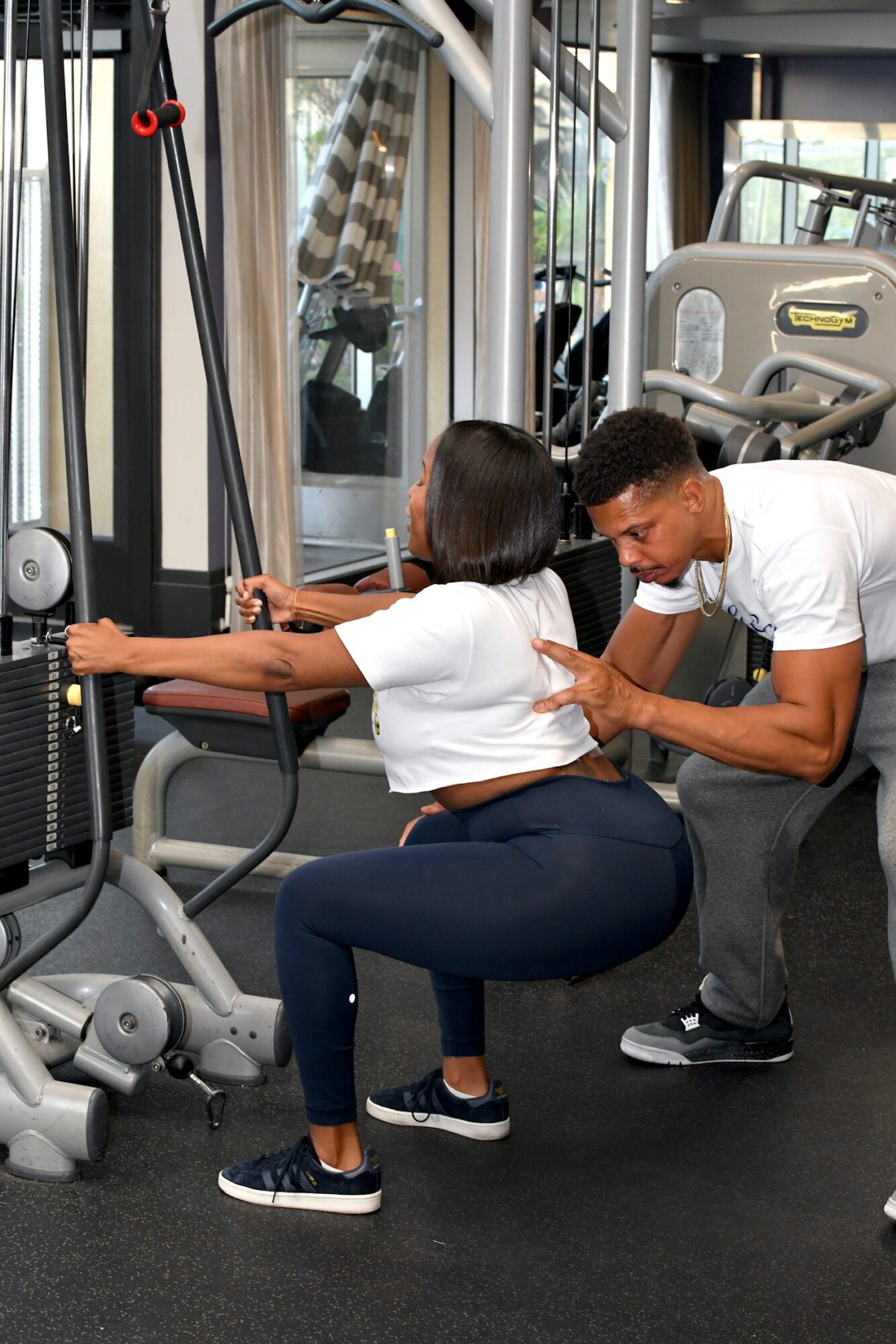 Personal trainer assisting a woman with a cable machine exercise in a gym, both focused on the workout.