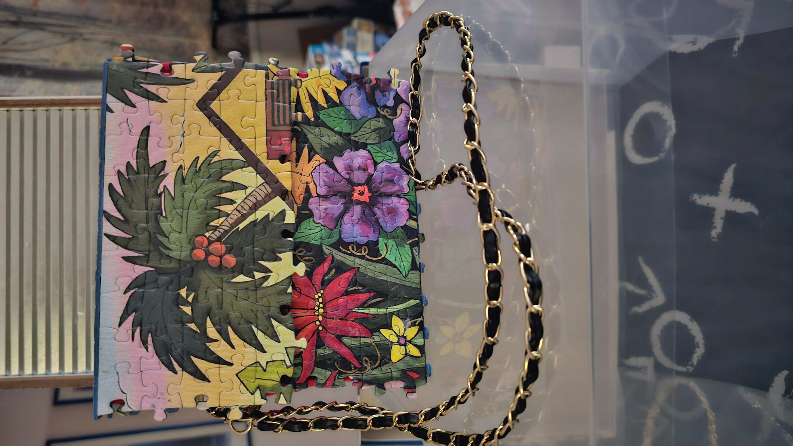 Colorful handbag with floral and leaf patterns, chain strap, and a rectangular shape, displayed on a surface.