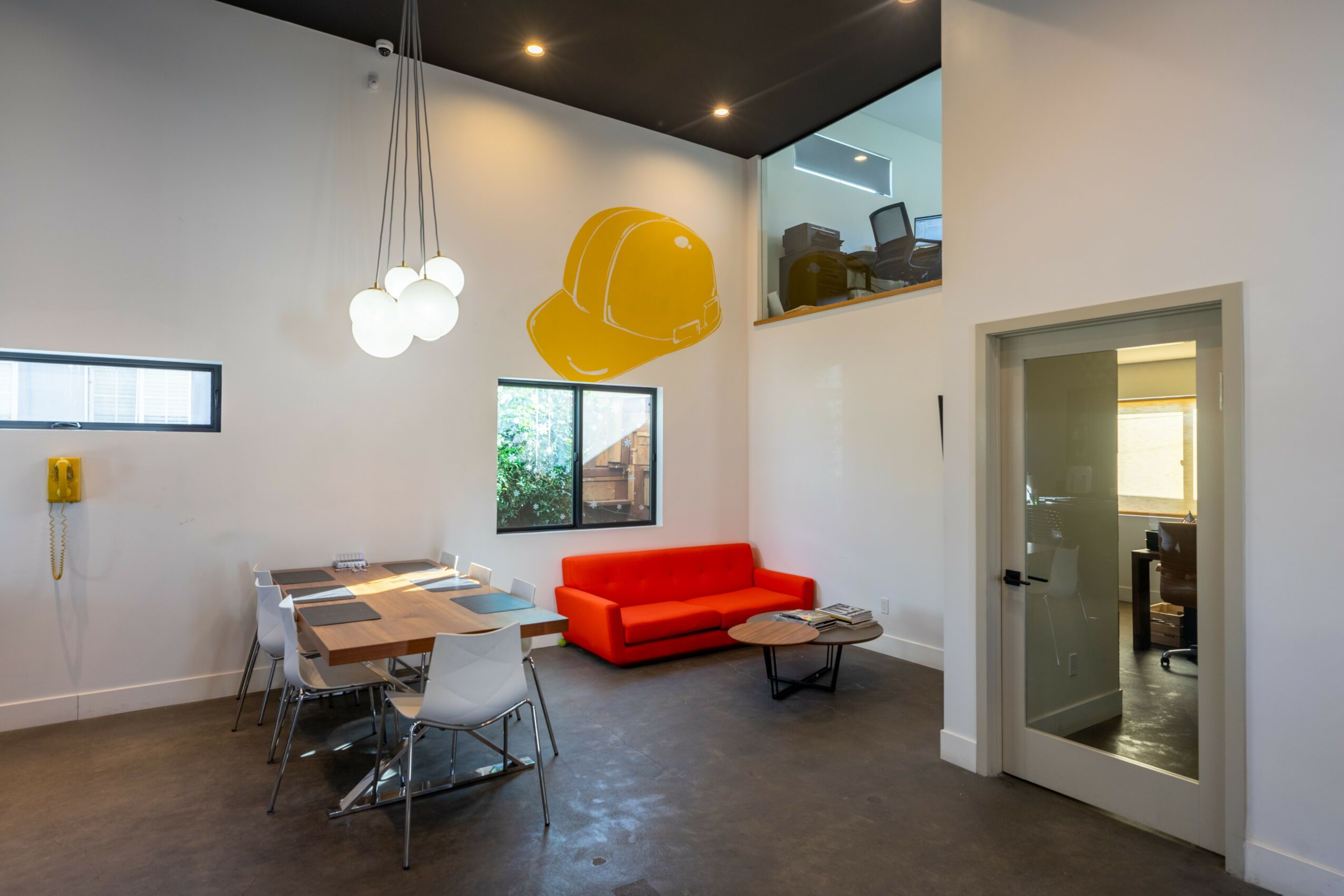 Modern interior with a red sofa, dining table, hanging light fixtures, and a yellow helmet sculpture on the wall.