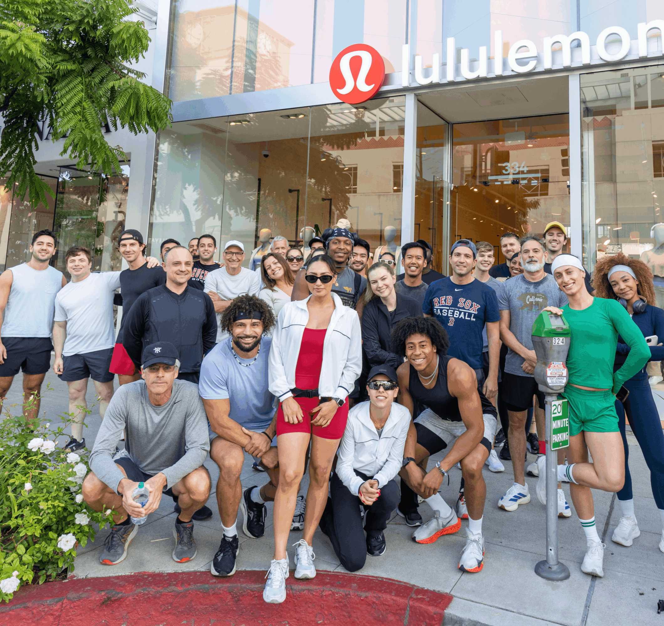 Group of people standing outside lululemon store, some smiling, some wearing athletic clothing, in front of glass storefront.