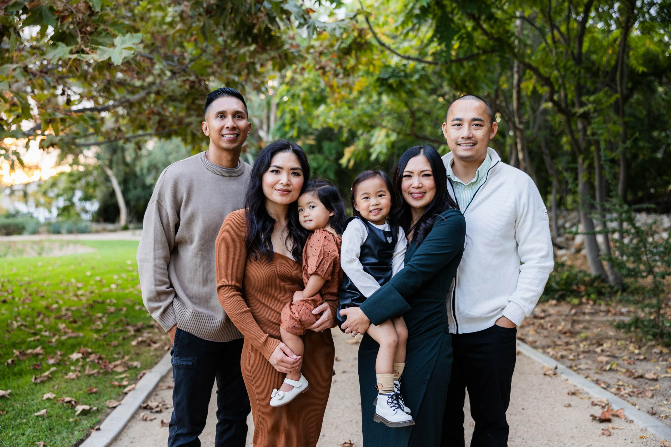 Group of six people, including children, standing outdoors on a path surrounded by trees and greenery.