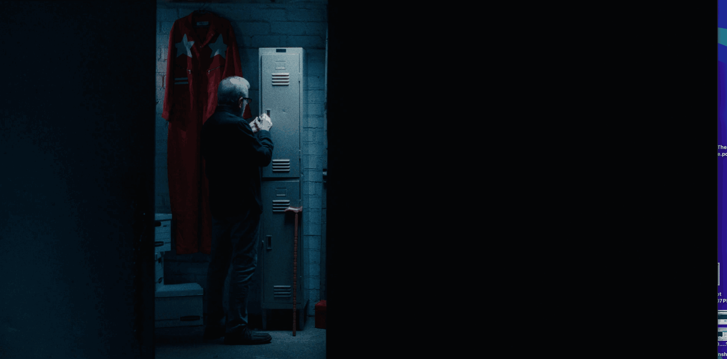 Person standing in front of lockers, holding a phone, in a dimly lit room with a red curtain and a blue wall.