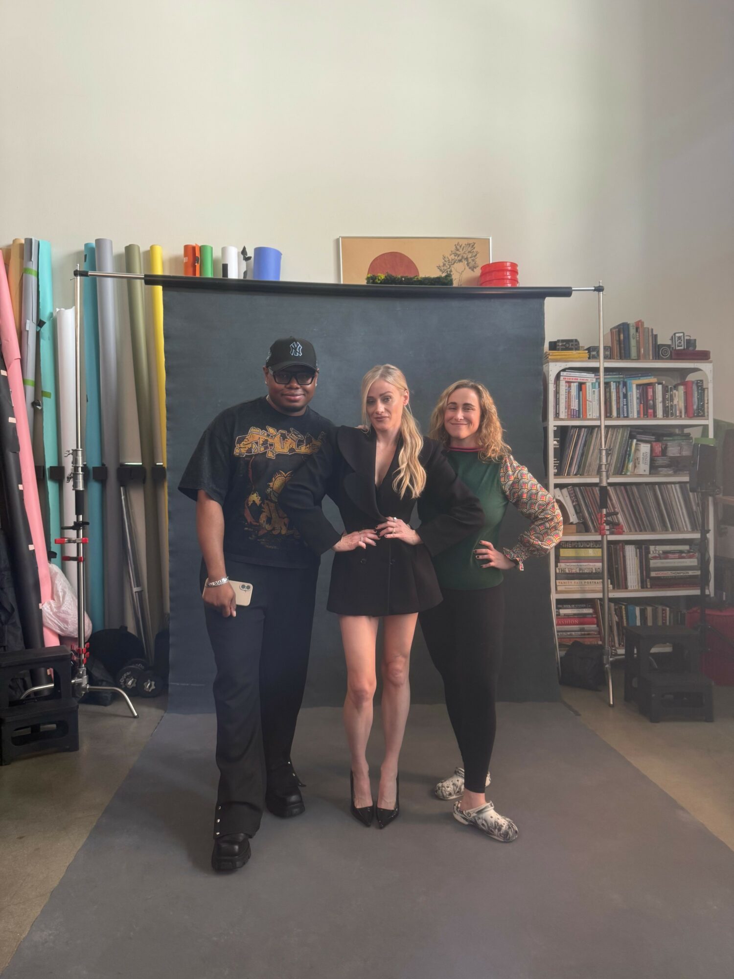 Three people standing in a room with shelves and equipment, one person holding a paper, two women smiling, one man wearing a cap.