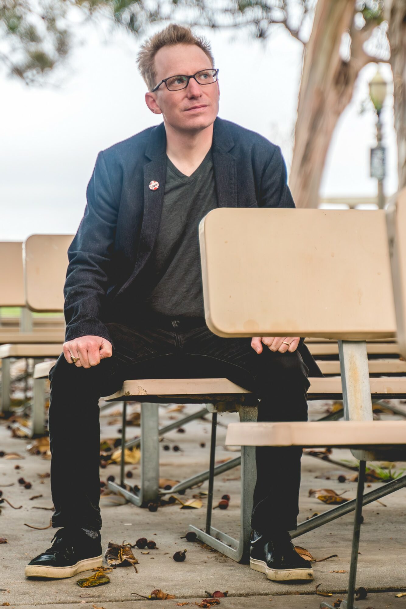 Person sitting on a bench outdoors holding a blank sign, with trees and a lamp post in the background.