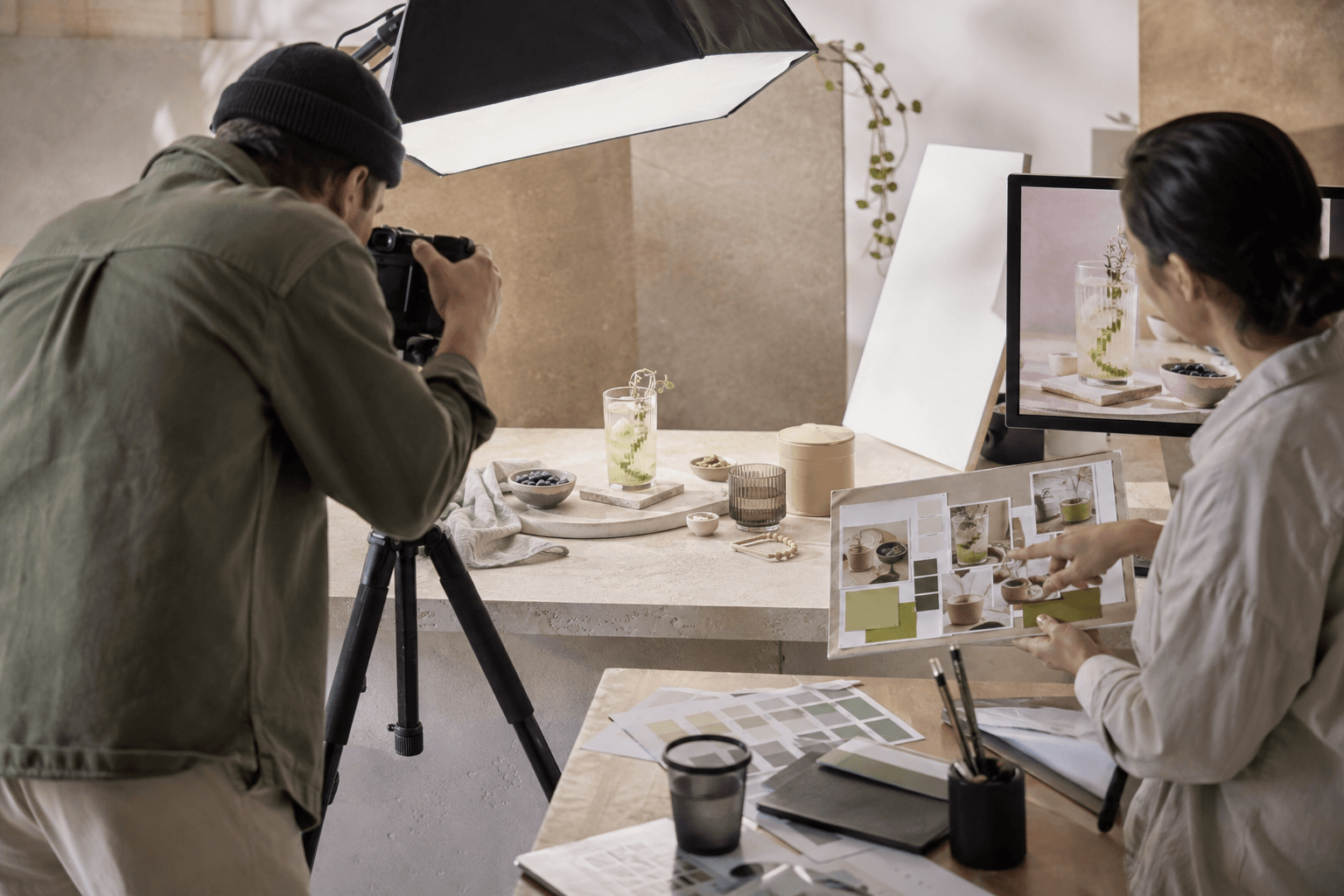 Photographer taking pictures of a woman working on a computer in a studio with photography equipment and props.