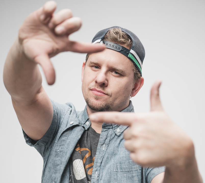 Young man with a cap making a framing gesture with his hands, looking at the camera, neutral background.