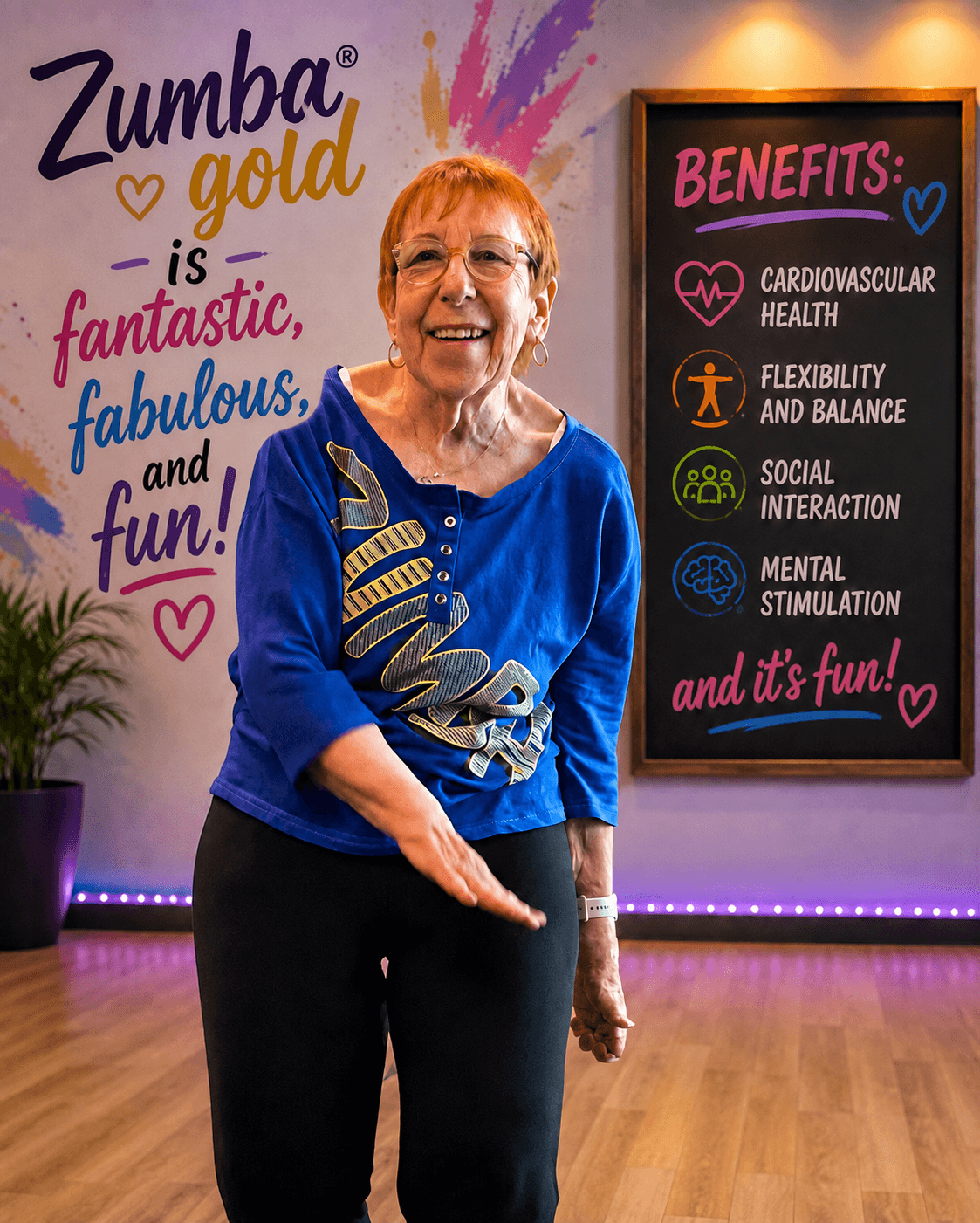 Smiling woman in blue top standing in Zumba studio with colorful wall art and benefits board, pointing downward. Word art and benefits list visible.