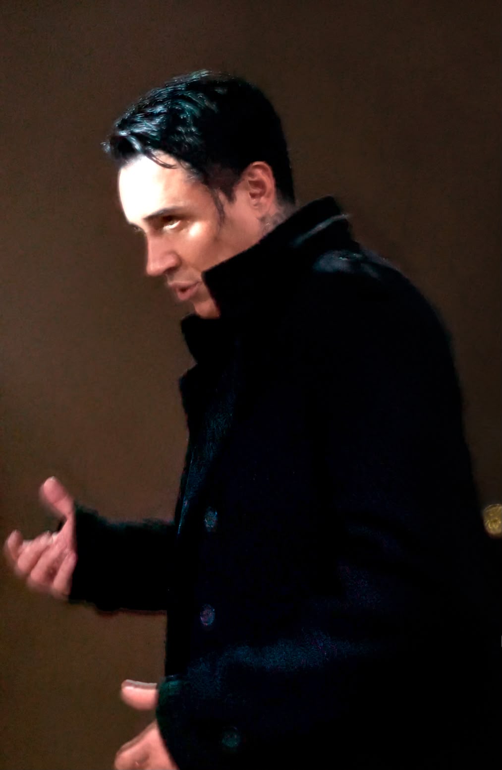 Man with dark hair and black clothing looking sideways, with a dark background.