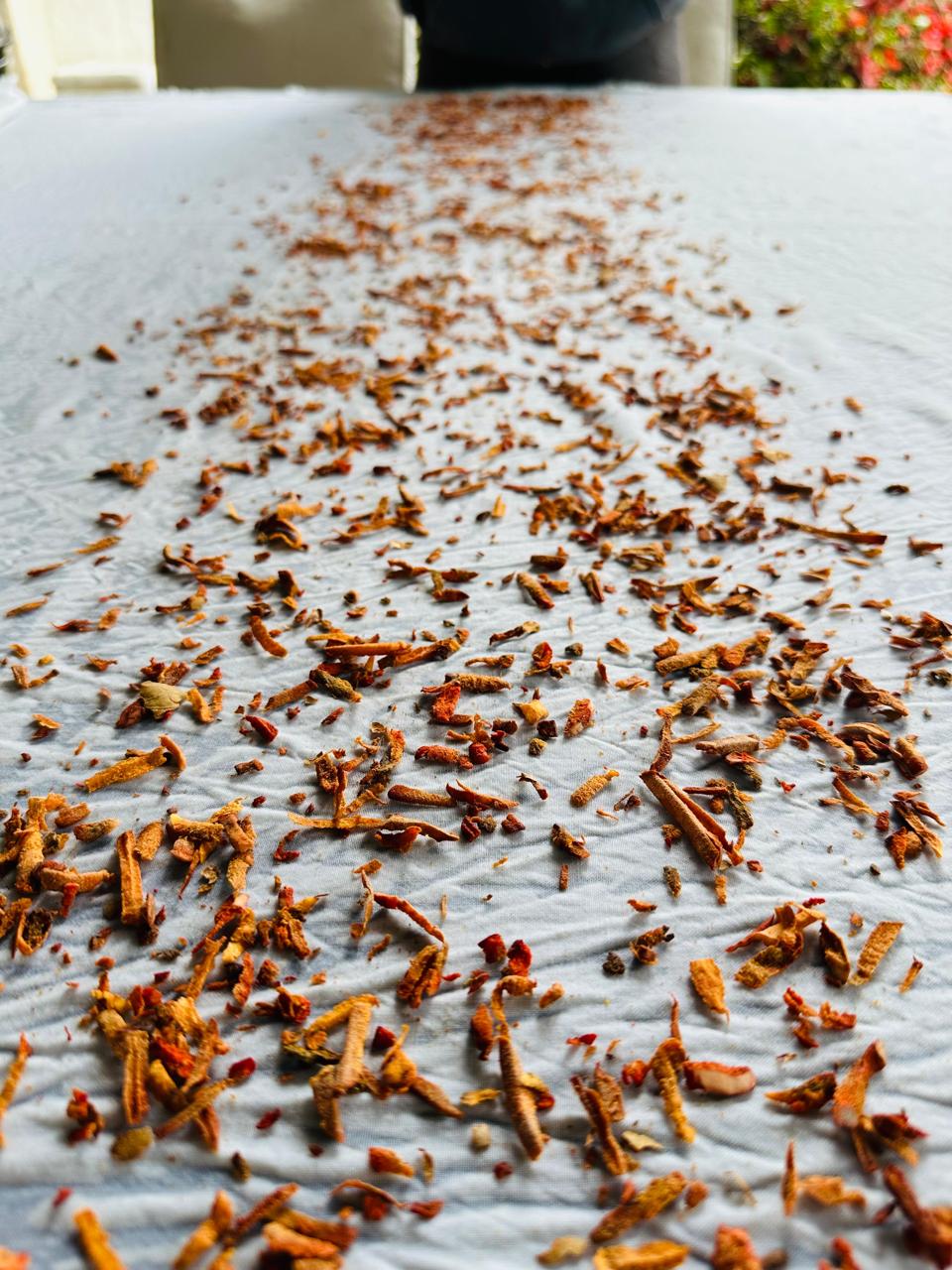 Dried orange peel scattered on a white surface outdoors, with a blurred background of plants and sky.