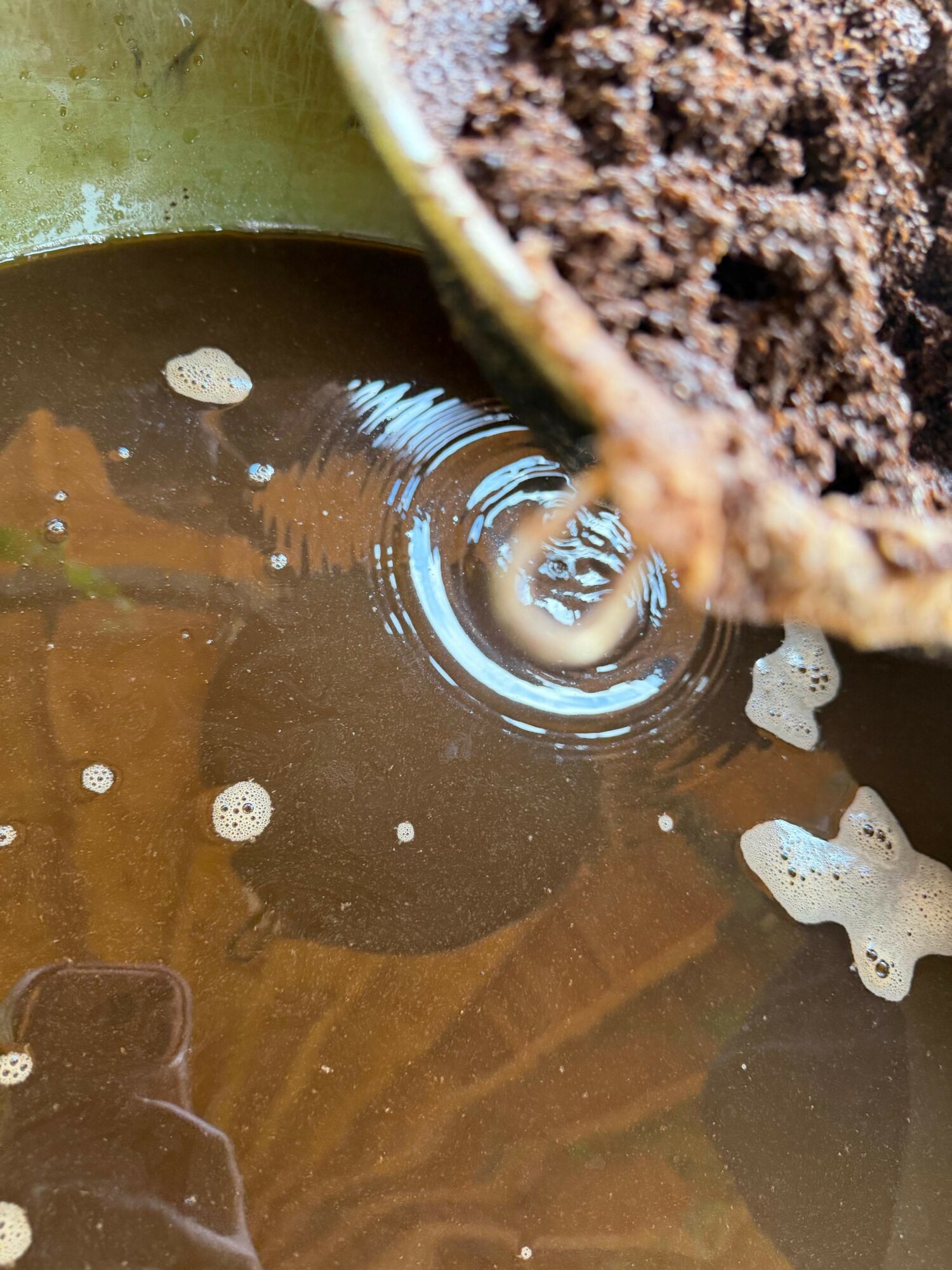 Close-up of a small pool of water with bubbles and ripples, partially covered by a soil-filled container edge.