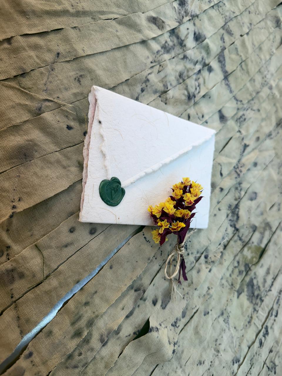 A slice of cake with white frosting, decorated with a green heart-shaped topper and yellow flowers, on a textured surface.