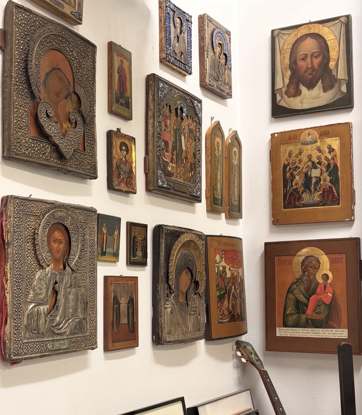 Collection of religious icons and paintings on a white wall, including images of Jesus and saints, arranged in various sizes and frames.