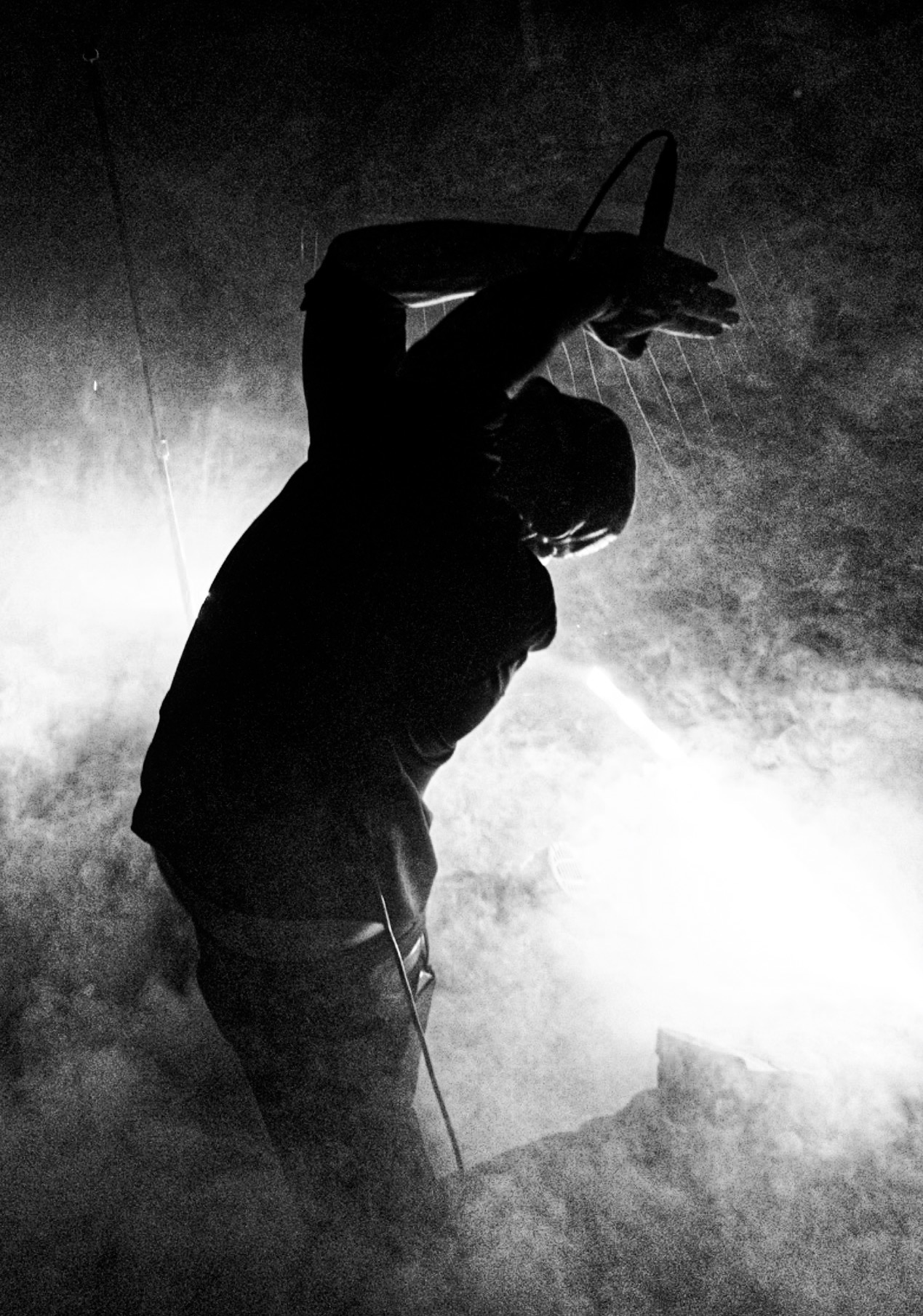 Silhouette of a person with arms raised, holding an object, against a smoky background, in black and white.