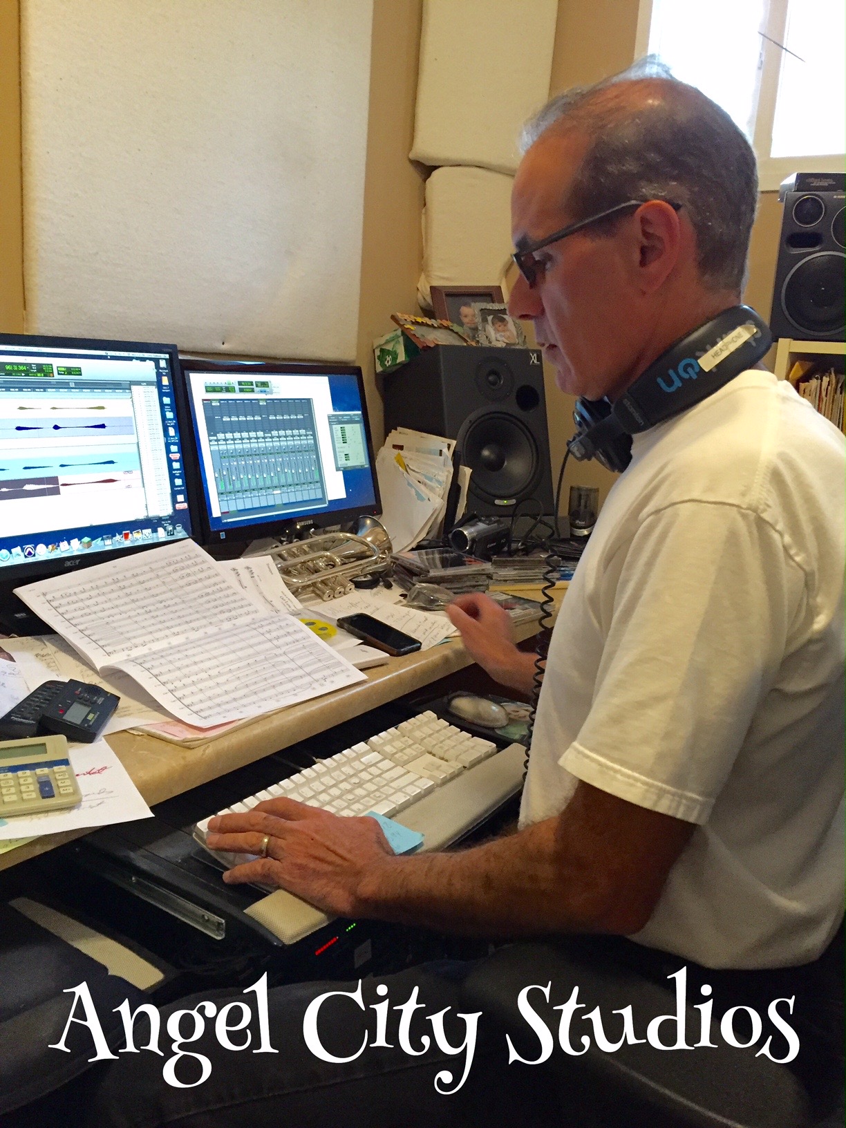 Man working at a music production station with multiple monitors, keyboard, and audio equipment in a studio.