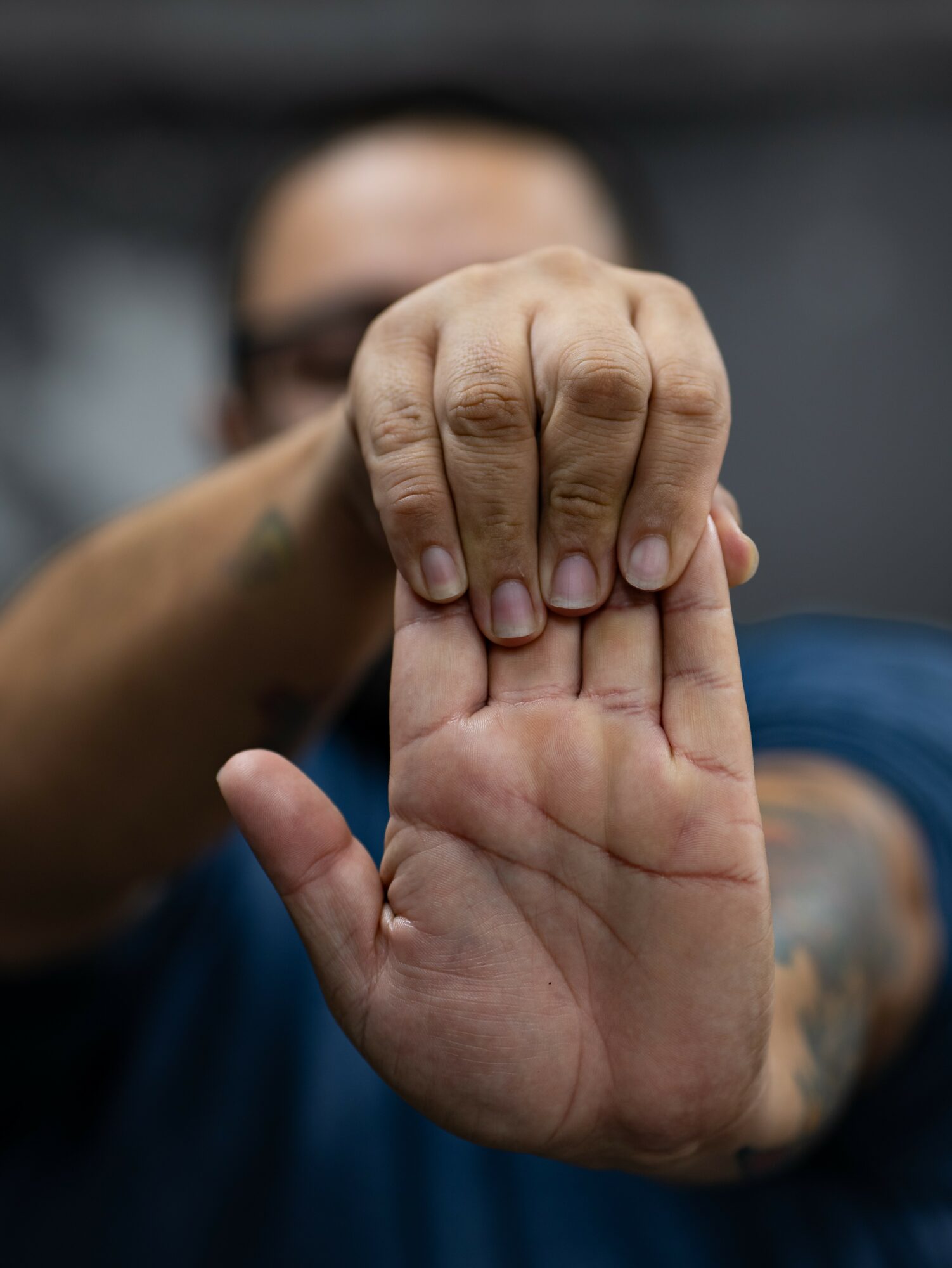 Person holding up a hand with fingers extended, focus on the hand, blurred face in background.