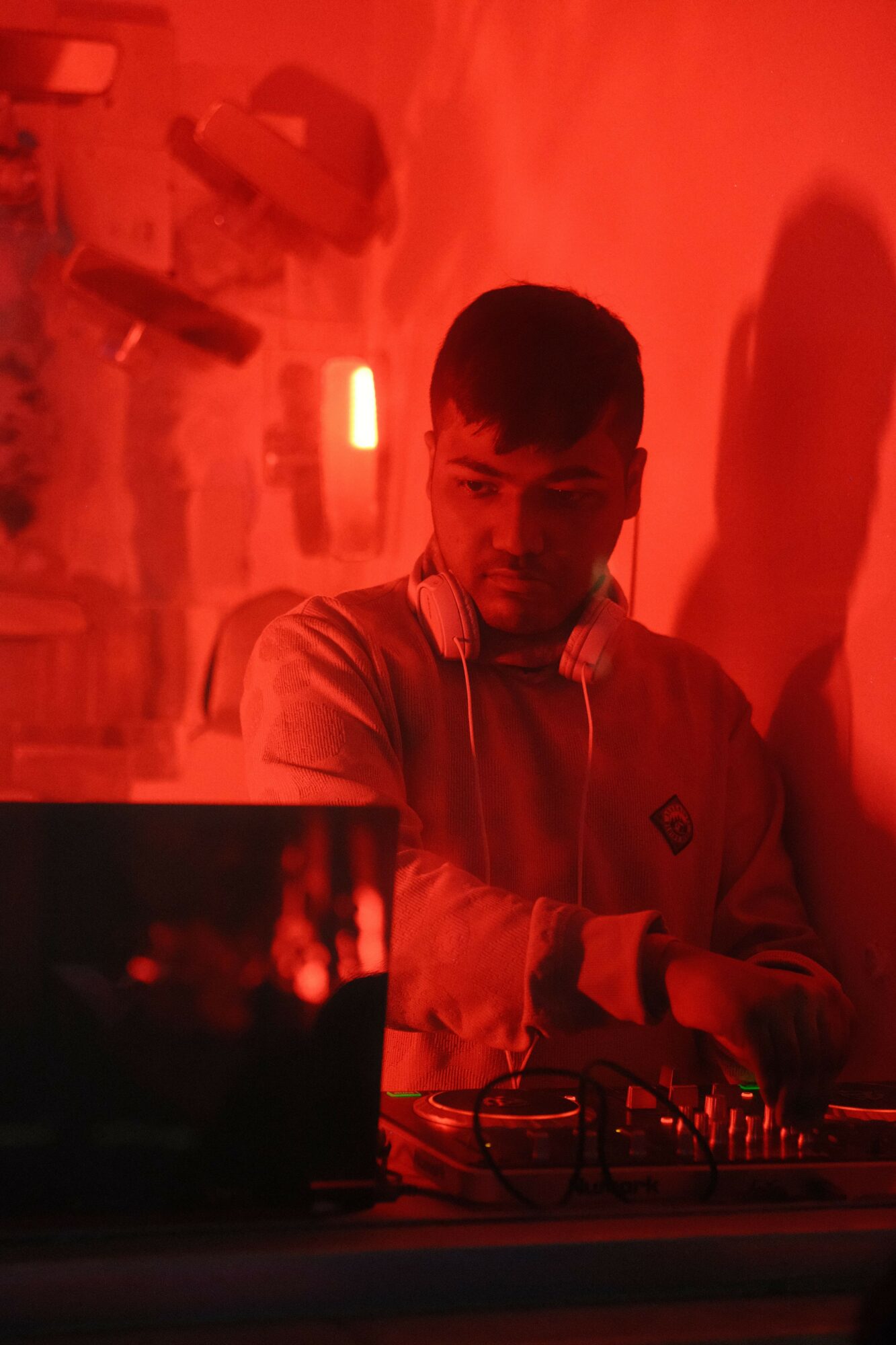 Person DJing with equipment in a red-lit environment, facing left, with a blurred background.