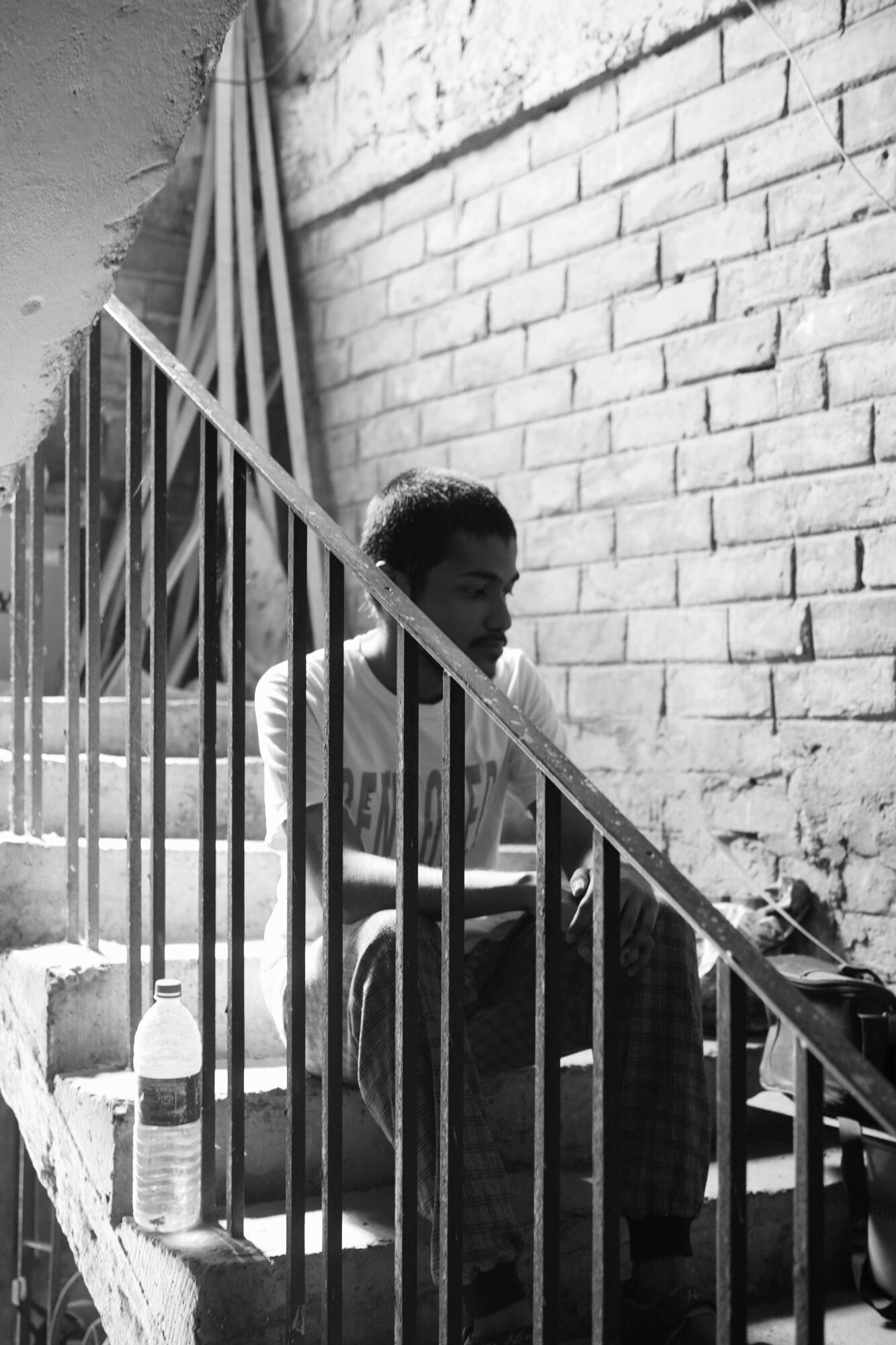 Person sitting on stairs next to a brick wall, with a water bottle nearby, in black and white.