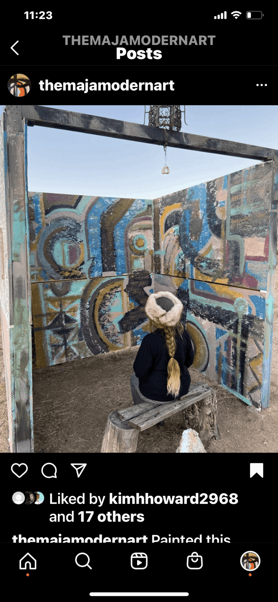 Person sitting on a bench in front of colorful abstract mural with swirling patterns and shapes, outdoor setting.