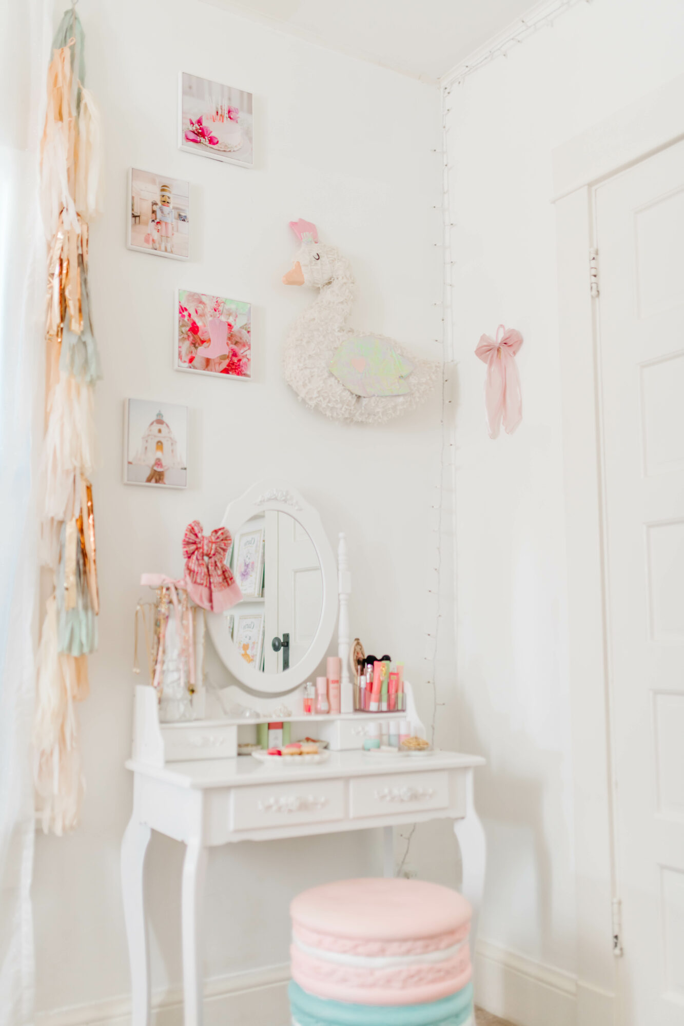White vanity with mirror, pink cushion, and decorative items in a bright, decorated room with wall art and hanging ornaments.