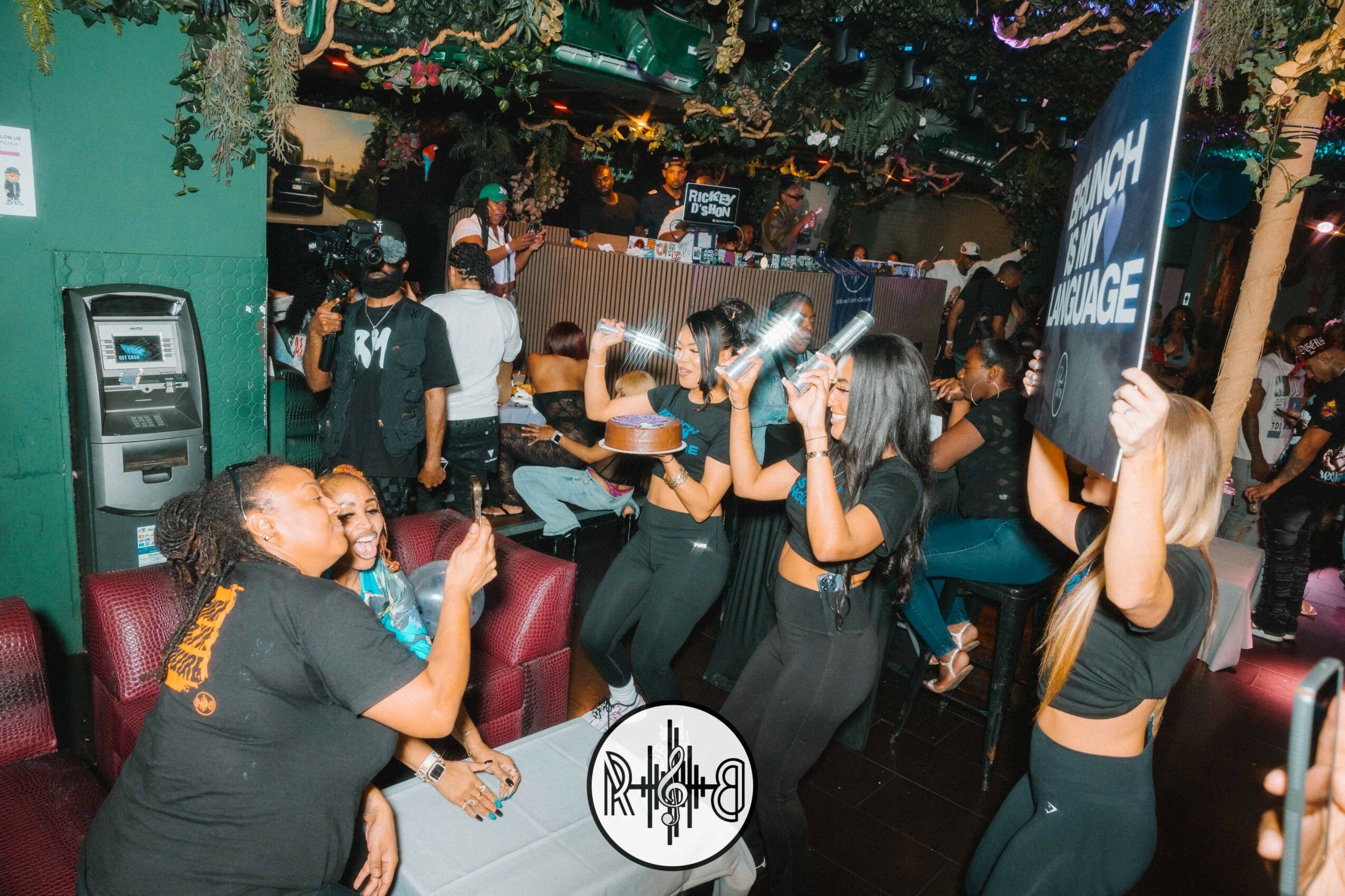 People dancing and socializing in a lively indoor venue with colorful decorations and a bar area in the background.