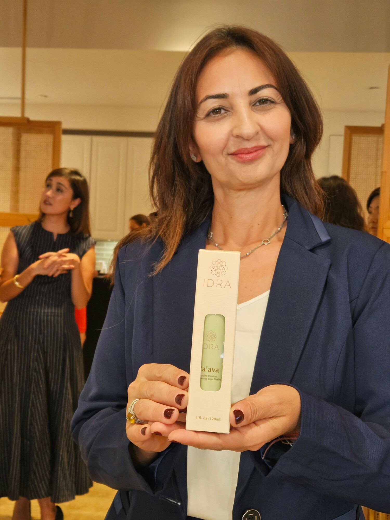 Woman with shoulder-length brown hair holding a certificate, smiling, wearing a dark blazer and white top, in an indoor setting.