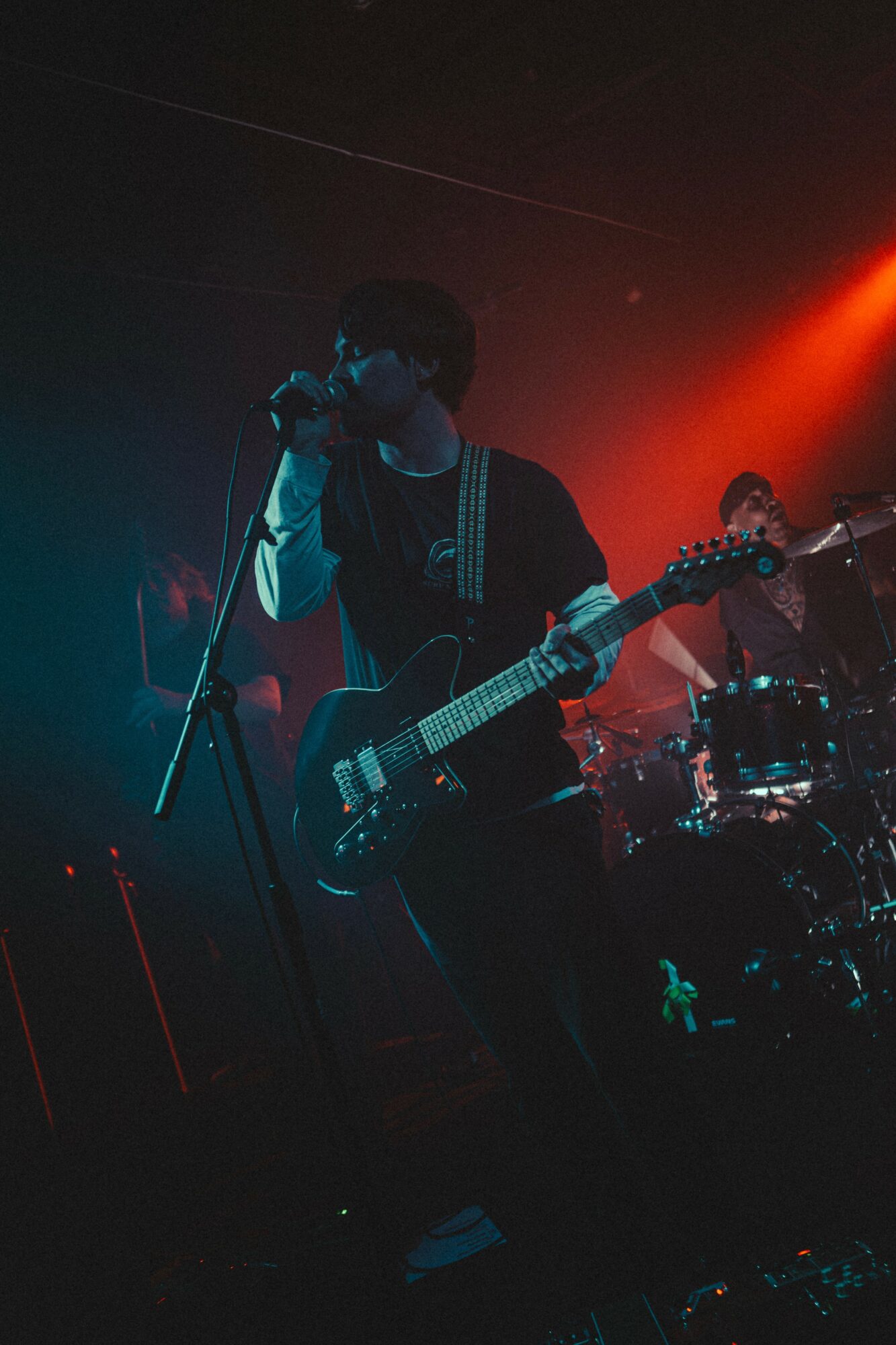 Person singing into a microphone and playing an electric guitar on stage with colorful lighting.