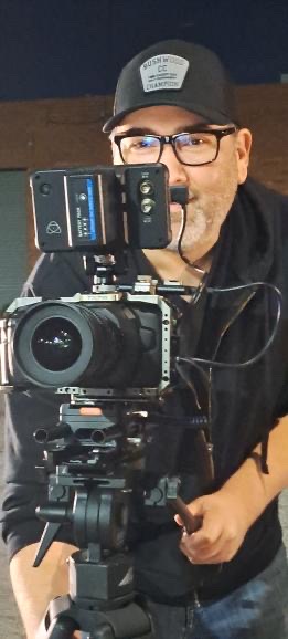 Person wearing glasses and a cap taking a photo with a professional camera, reflected in a mirror.