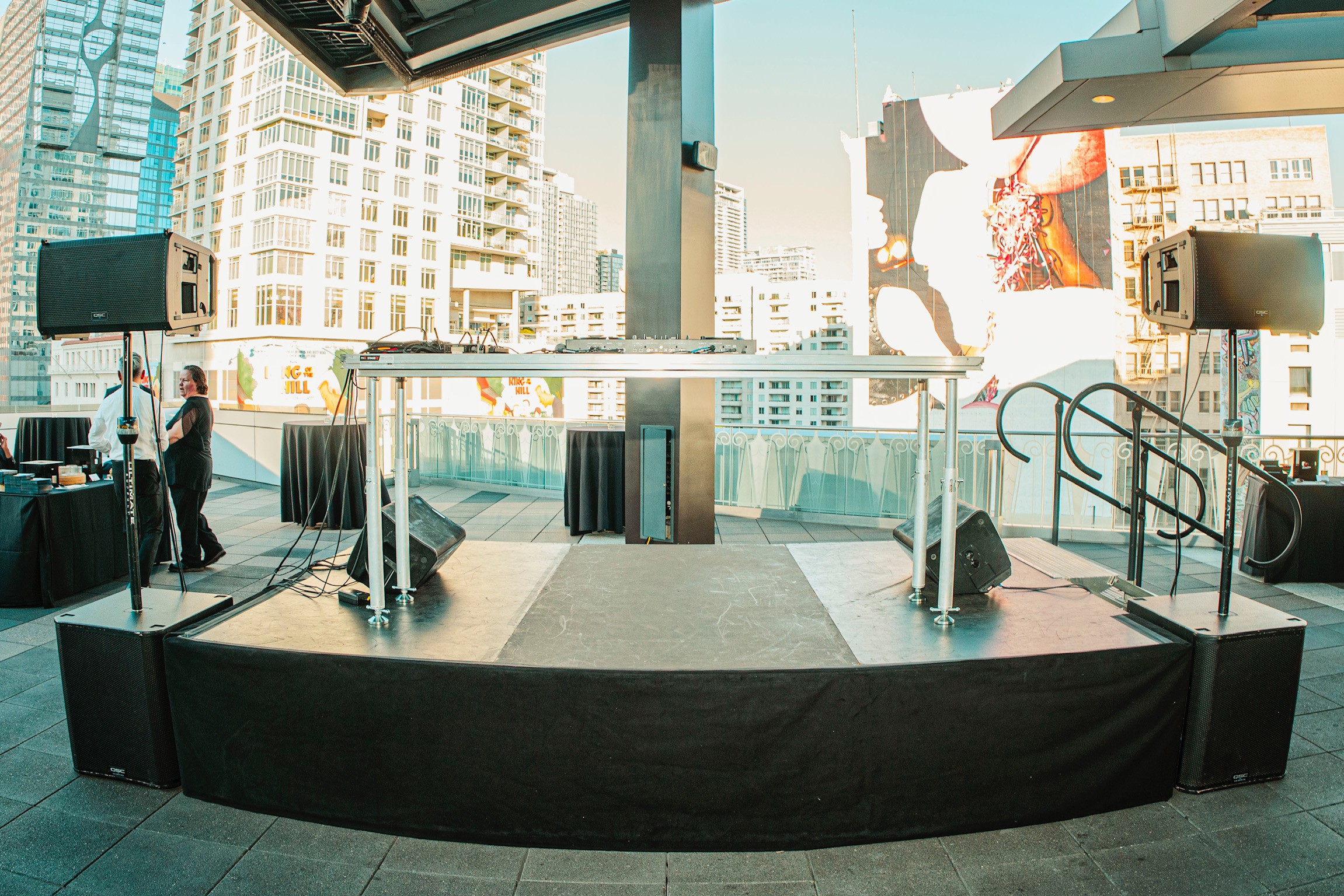 Stage setup with speakers and cityscape background, indoors with large windows and a city view, daytime.