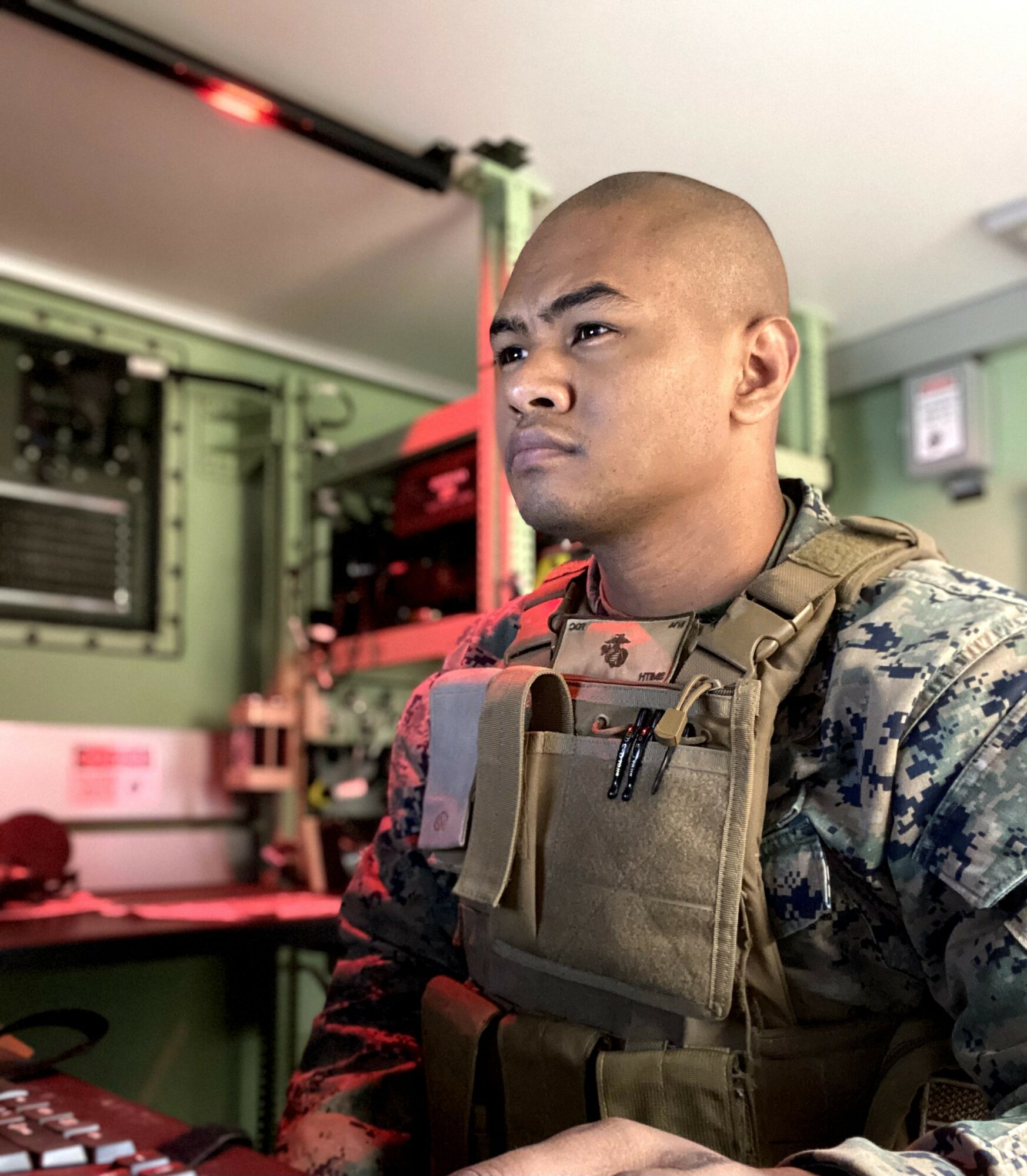 Military personnel in uniform with tactical gear in a room with green walls and equipment.