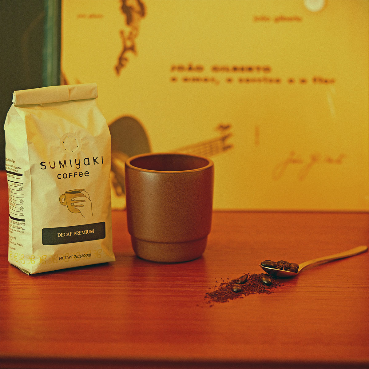 Coffee cup, spoon with coffee grounds, and a bag of Sumiyaki coffee on a wooden surface.