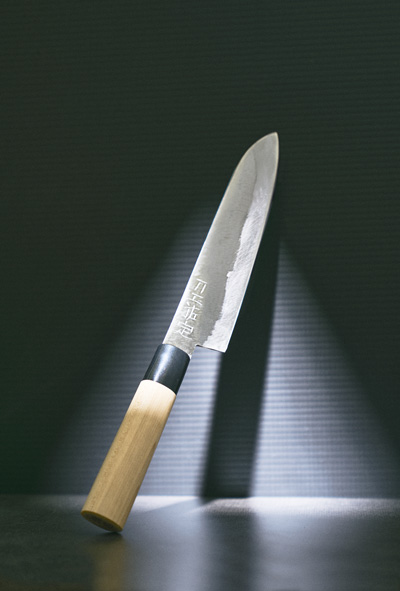 A kitchen knife with a wooden handle leaning against a dark background, casting a shadow on the surface.
