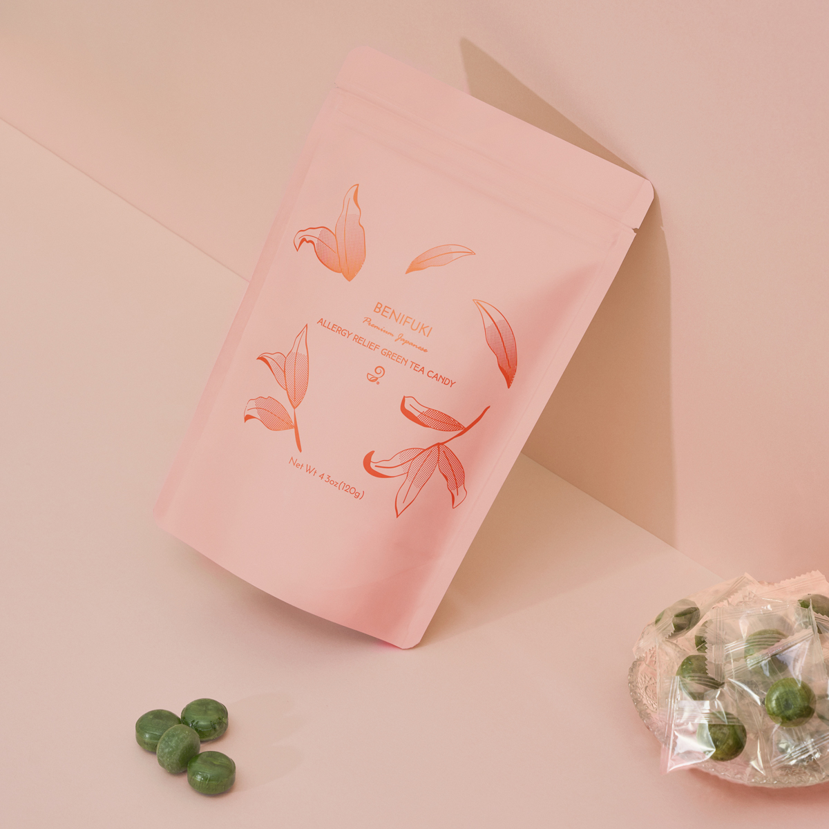 Pink package with floral design and text, three green candies in front, on a light background.