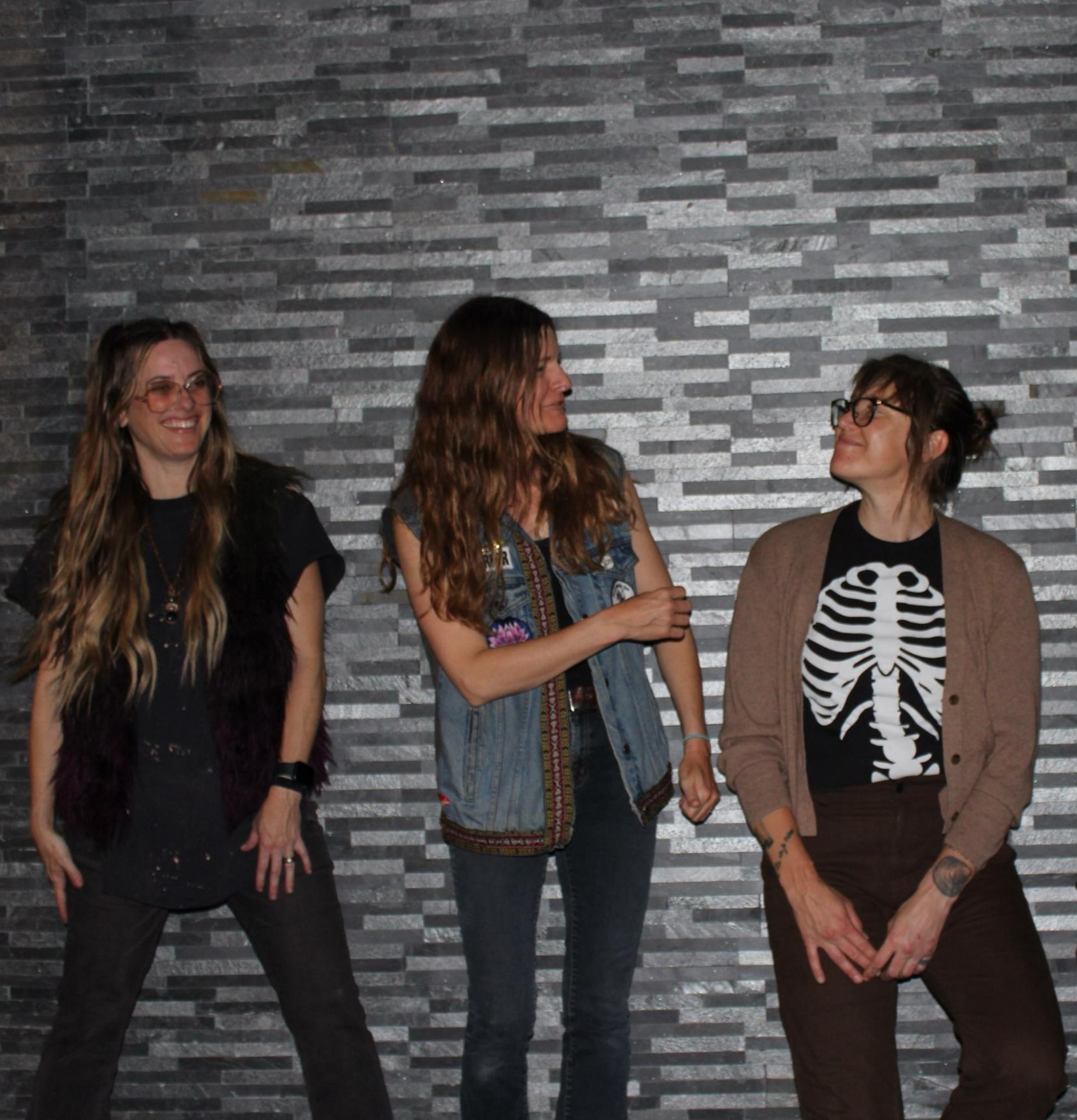 Three women standing and talking against a textured gray wall, smiling and engaging with each other.