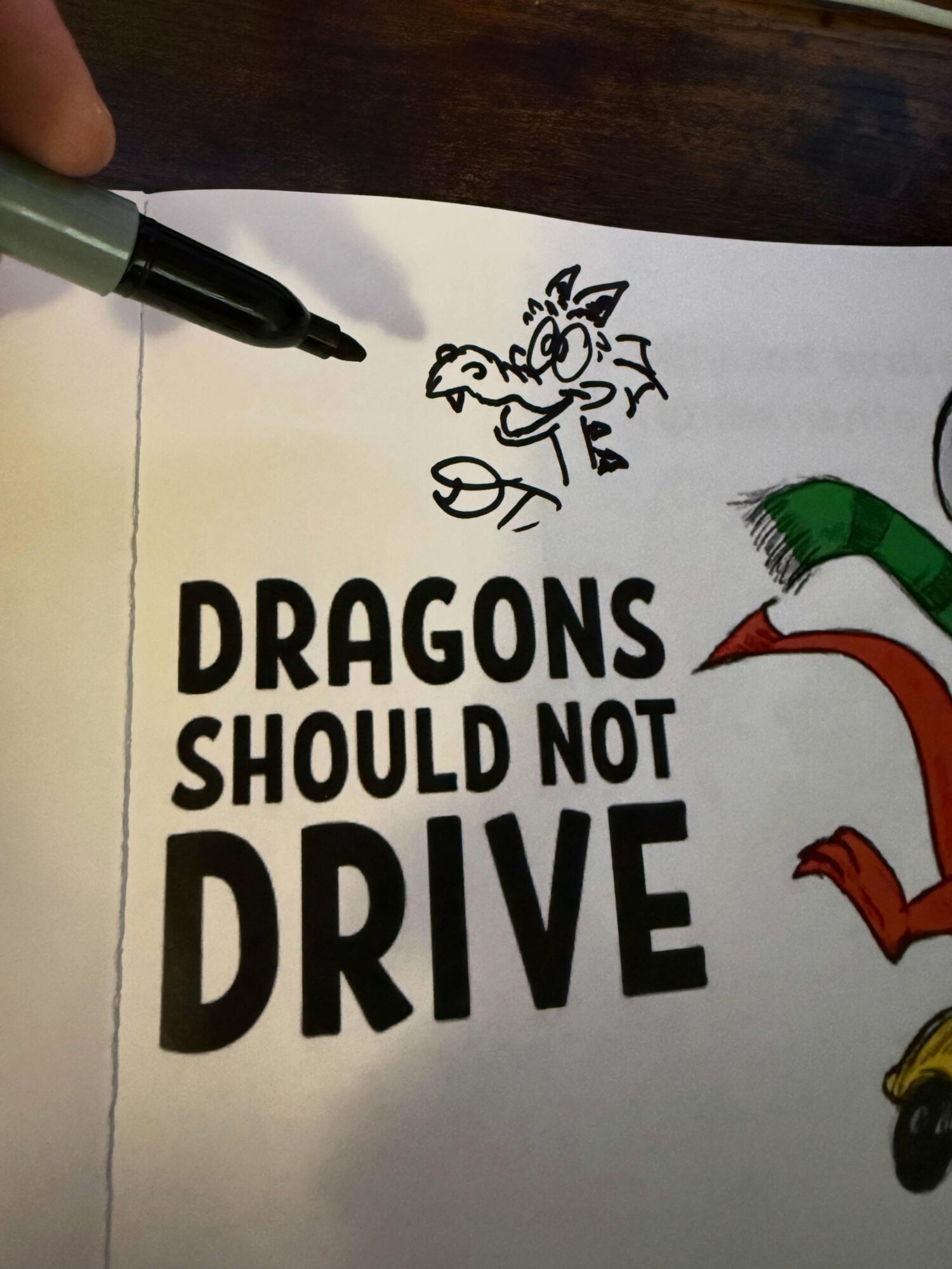Hand-drawn dragon cartoon above text, which reads 'DRAGONS SHOULD NOT DRIVE', on white paper.