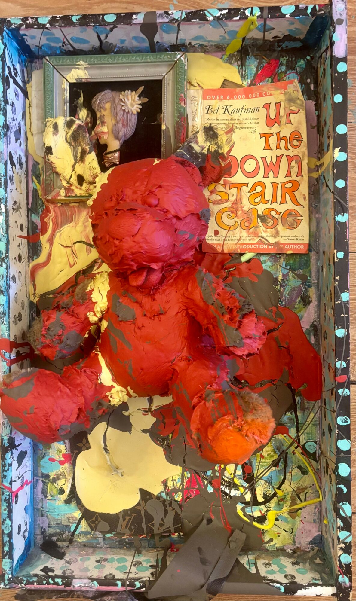 Mixed media art piece with red textured sculpture, framed photo, and colorful background, including a sign reading 'Up the Down Staircase'.