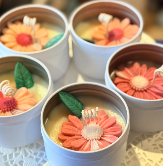 Five candles decorated with pink and orange flower designs, green leaves, and small white decorative elements in white containers.