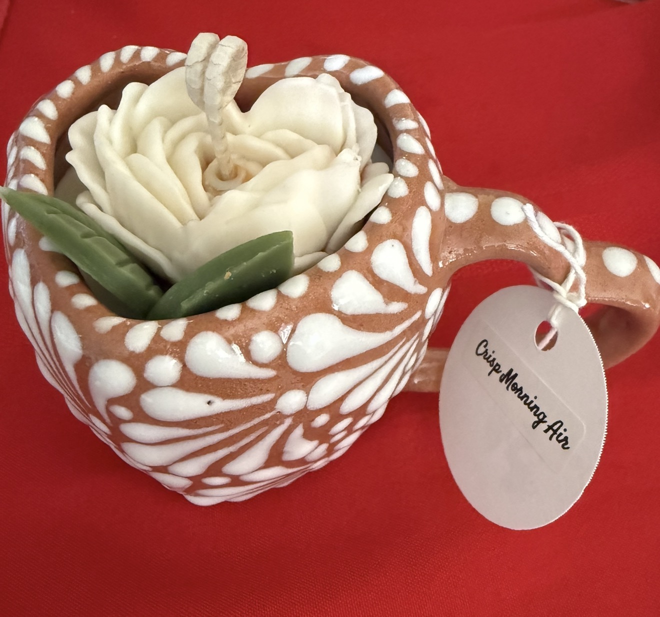 Decorative mug shaped like a gingerbread cookie with white icing, filled with cream and green leaves, on red background.