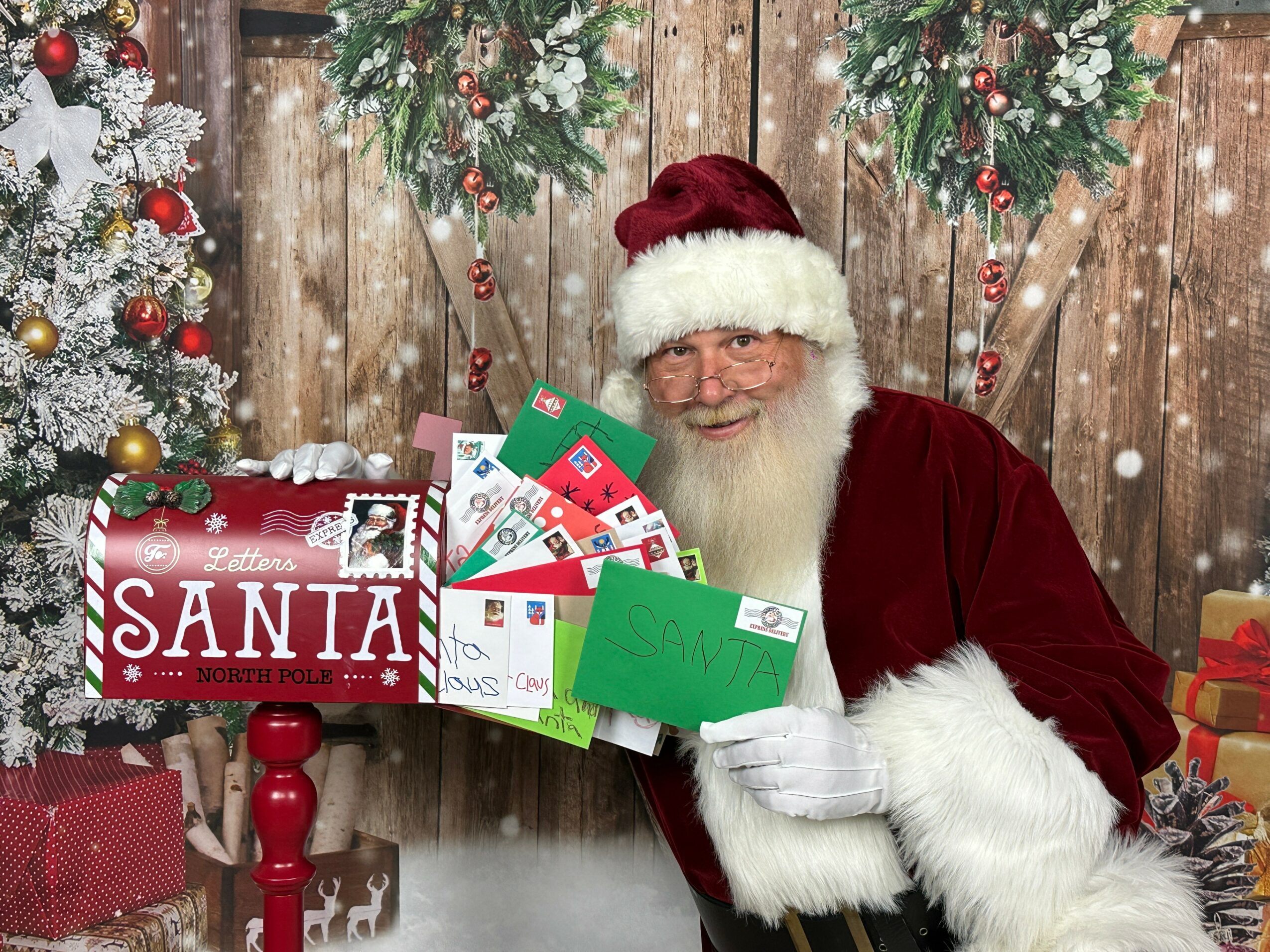 Santa Claus in a red suit and hat holding a green sign, surrounded by Christmas decorations and a gift box, with snow falling.